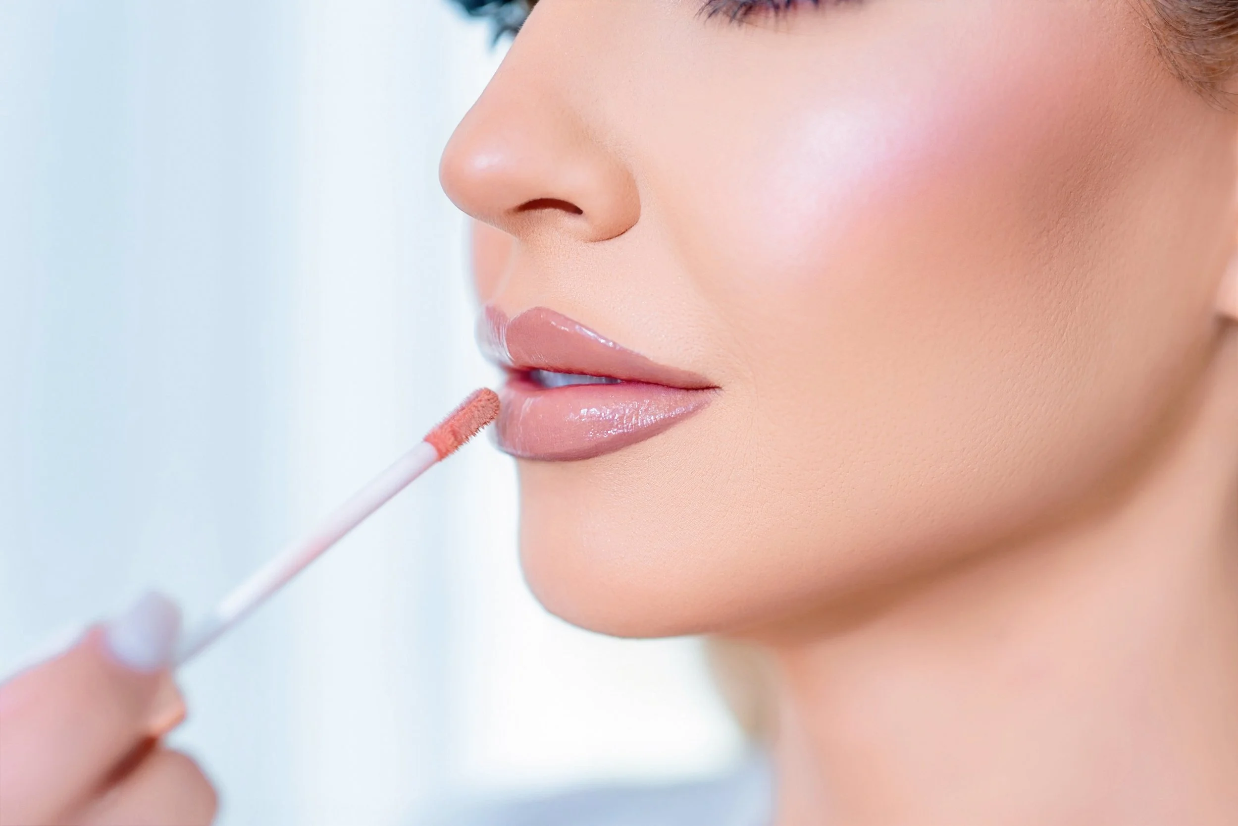 Close-up of a woman applying nude lipstick using a doe-foot applicator.