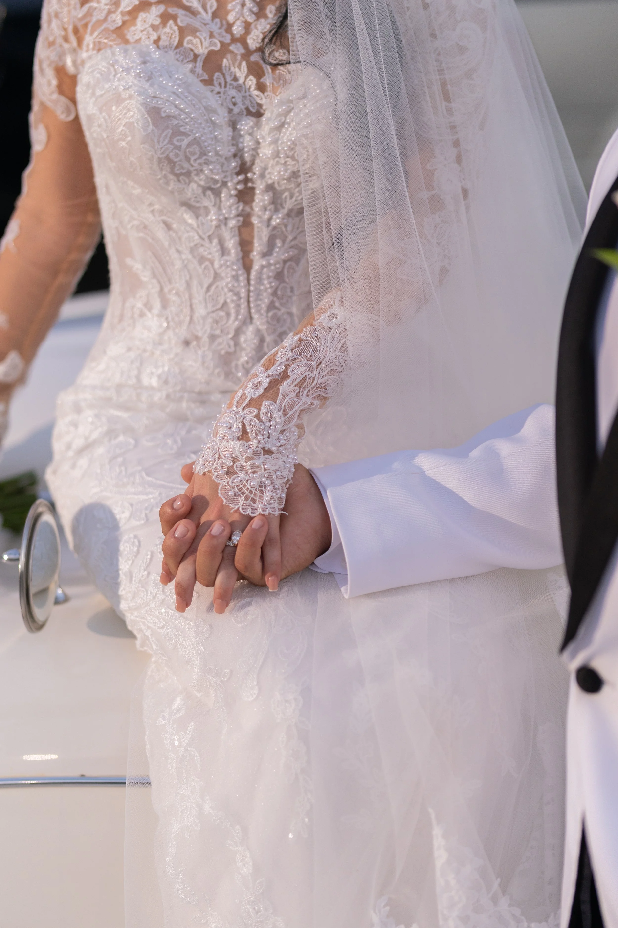 Bride and groom holding hands during wedding ceremony, with bride wearing a lace wedding dress and veil, and groom in a tuxedo.
