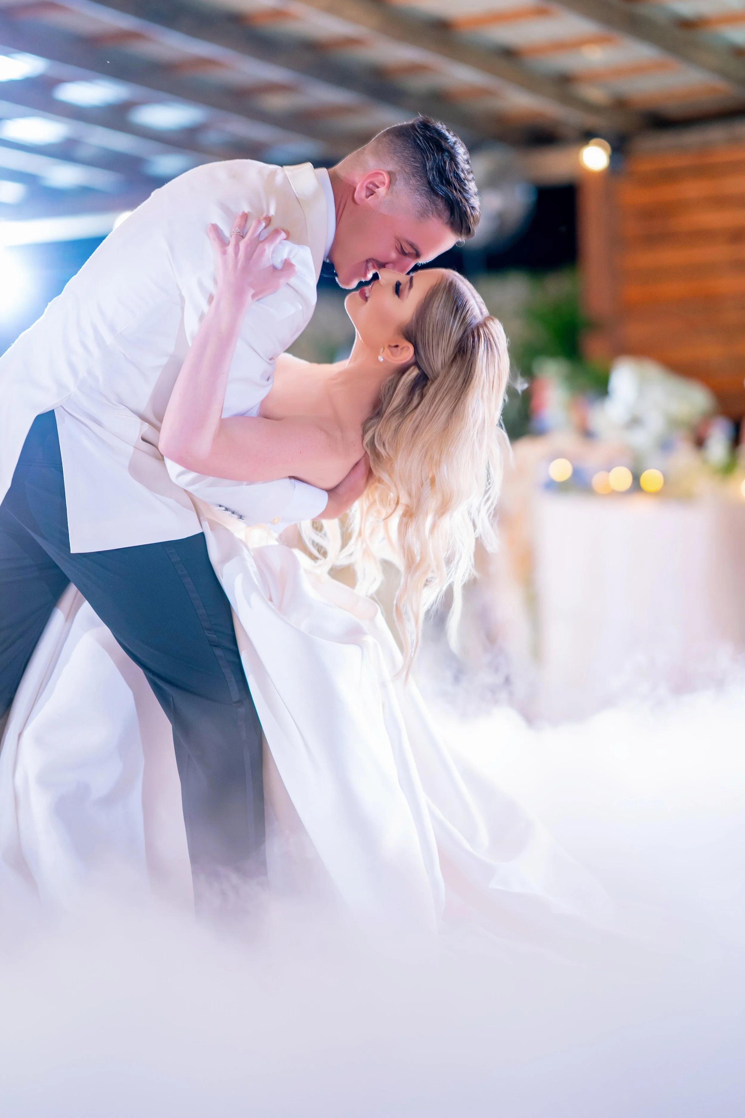 A couple dancing at a wedding, the man dipping the woman, both smiling and looking at each other.