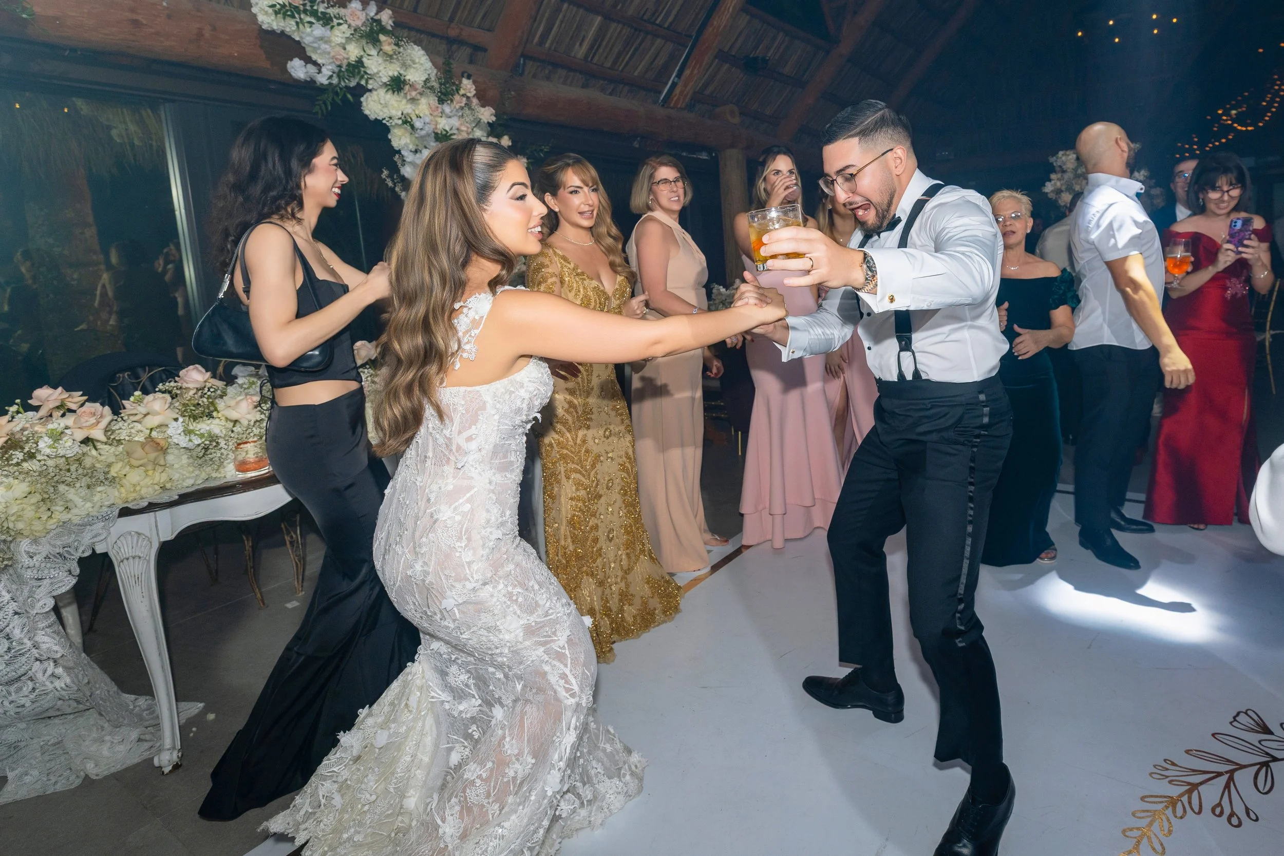A wedding reception with a bride and groom dancing and drinking with guests in the background at a decorated venue.