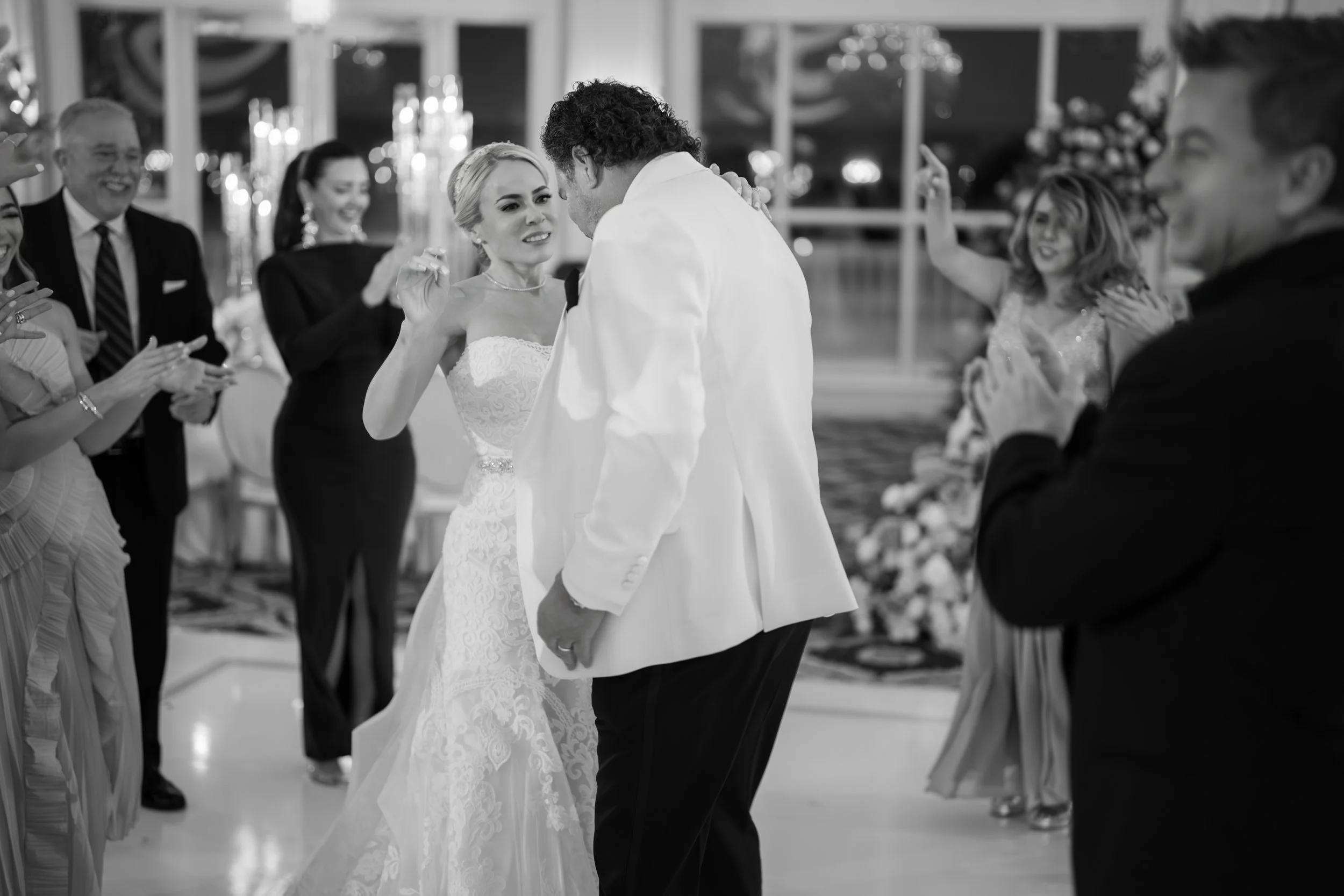 A bride and groom sharing a dance at their wedding reception, surrounded by family and friends cheering and clapping.