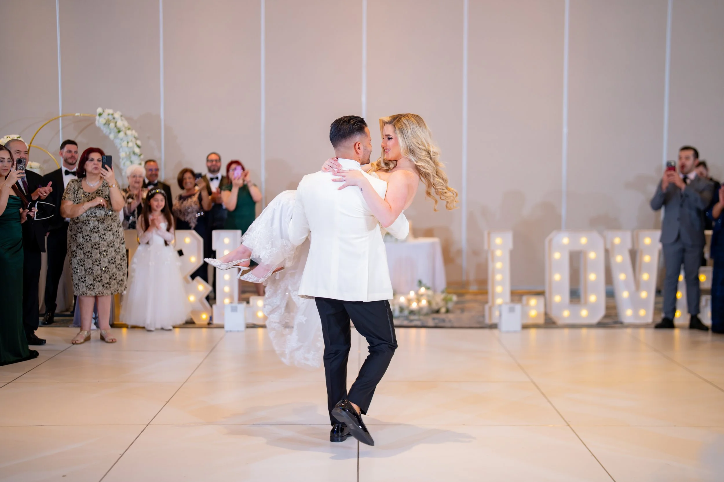 Groom lifting the bride in front of LOVE marquee letters at HILTON TAMPA DOWNTOWN; fun wedding reception highlights by Star Visual Art, Tampa.
