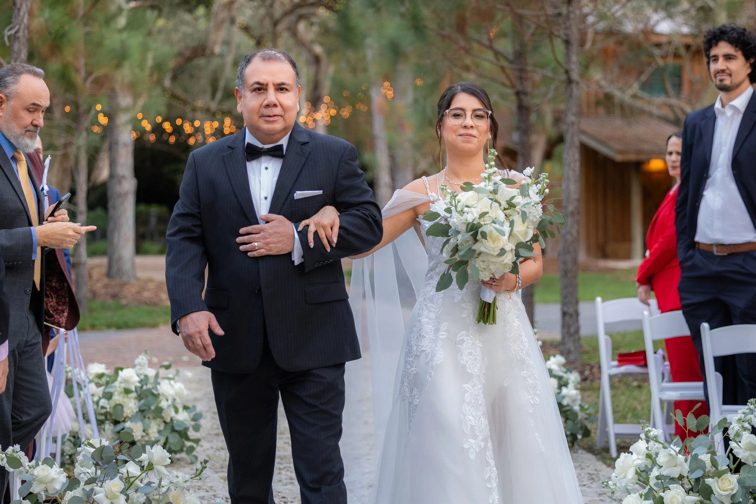 A bride walking down the aisle with her father at an outdoor wedding ceremony.
