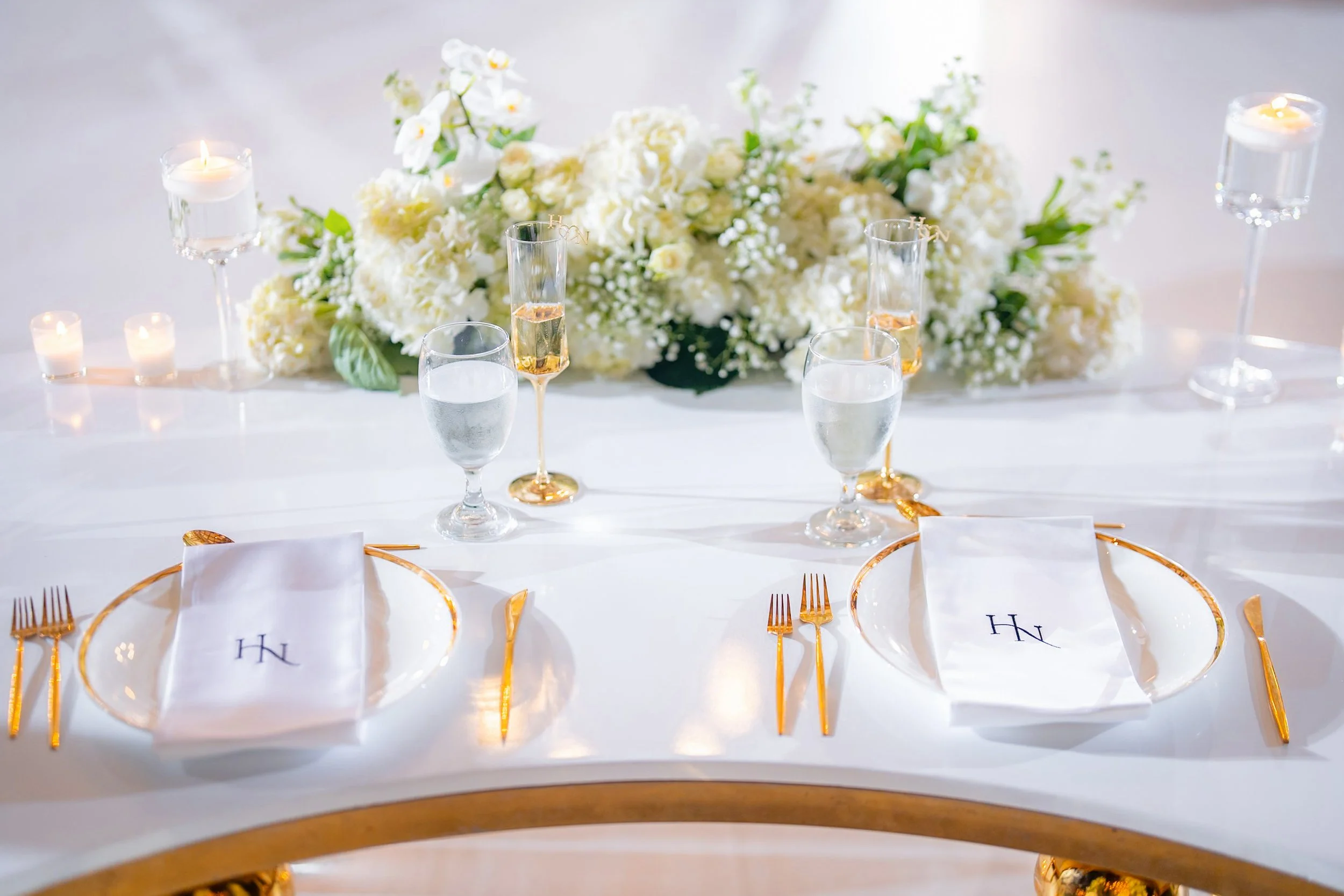 Elegant table setting with white floral centerpiece, candles, and gold-rimmed plates and cutlery for a formal event.