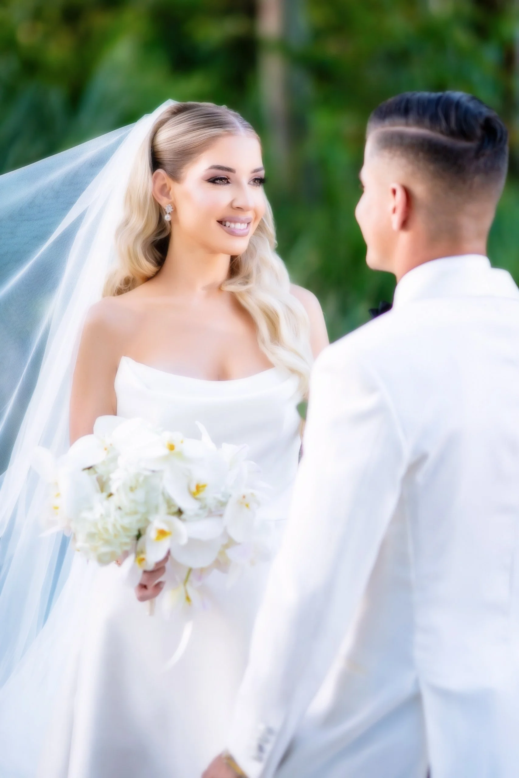 A bride and groom exchanging vows outdoors, with the bride holding a bouquet of white flowers and smiling at each other.