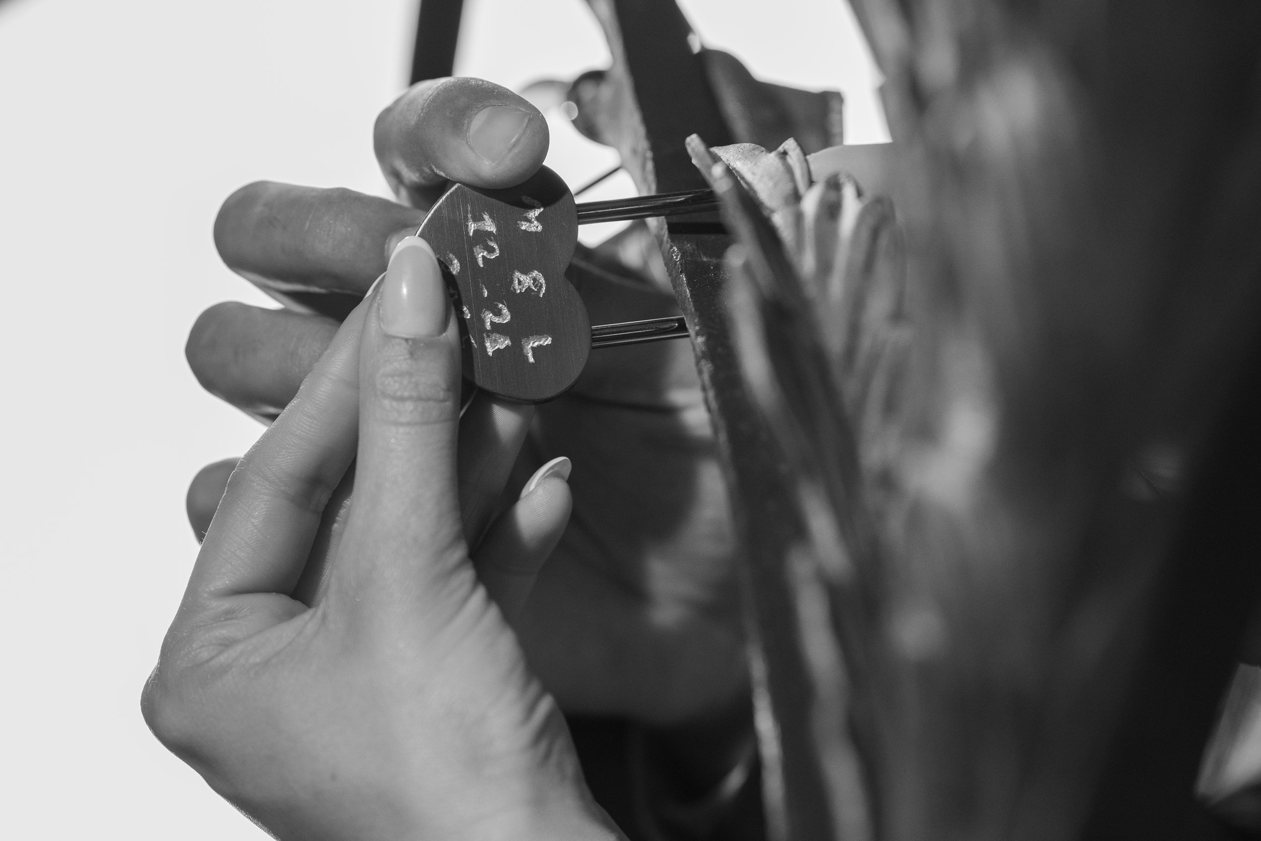 Close-up of a person's hand holding a small round chalkboard with numbers written on it, while using pins to attach it to a larger object, with blurred background.