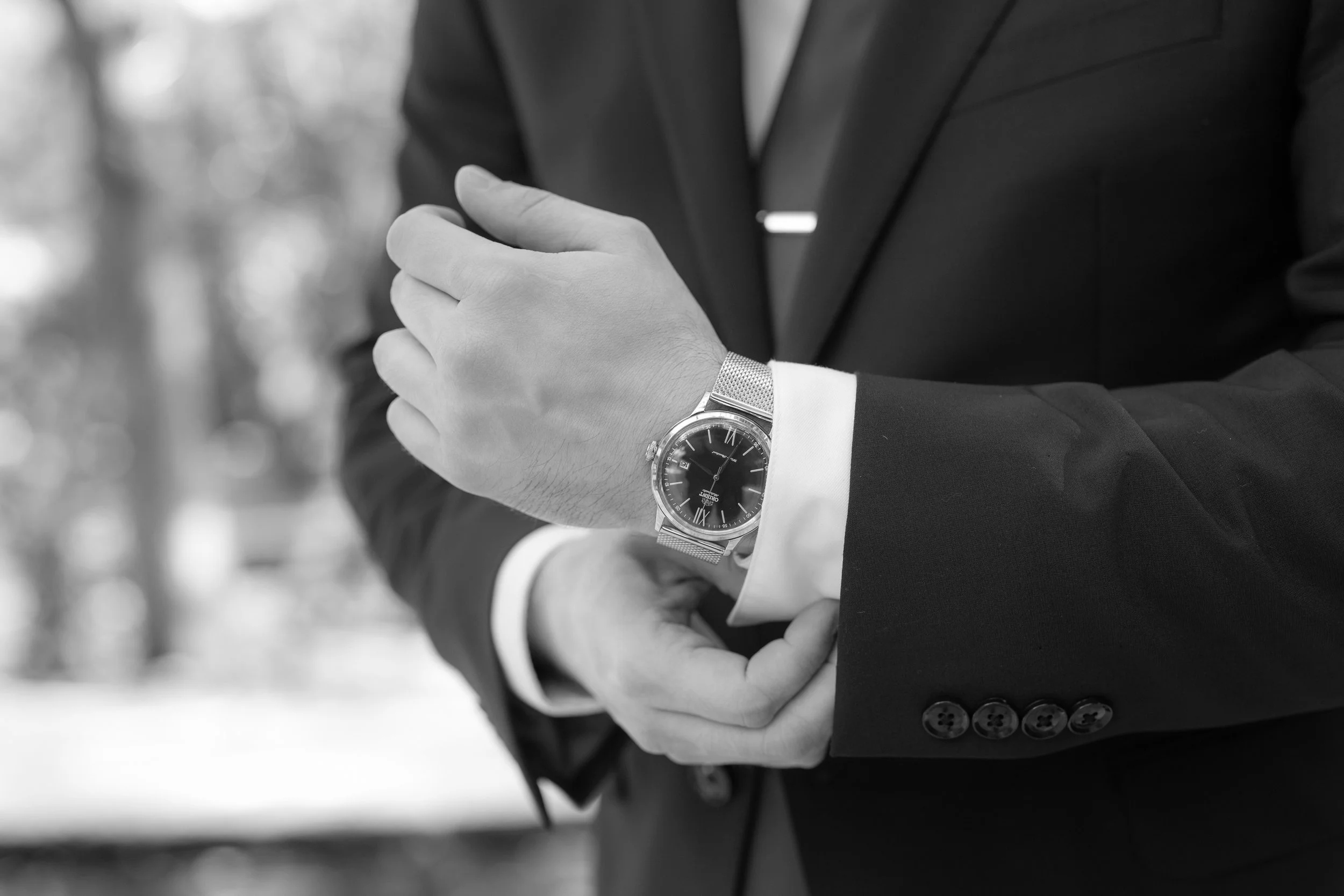 A man in a suit adjusting his wristwatch outdoors