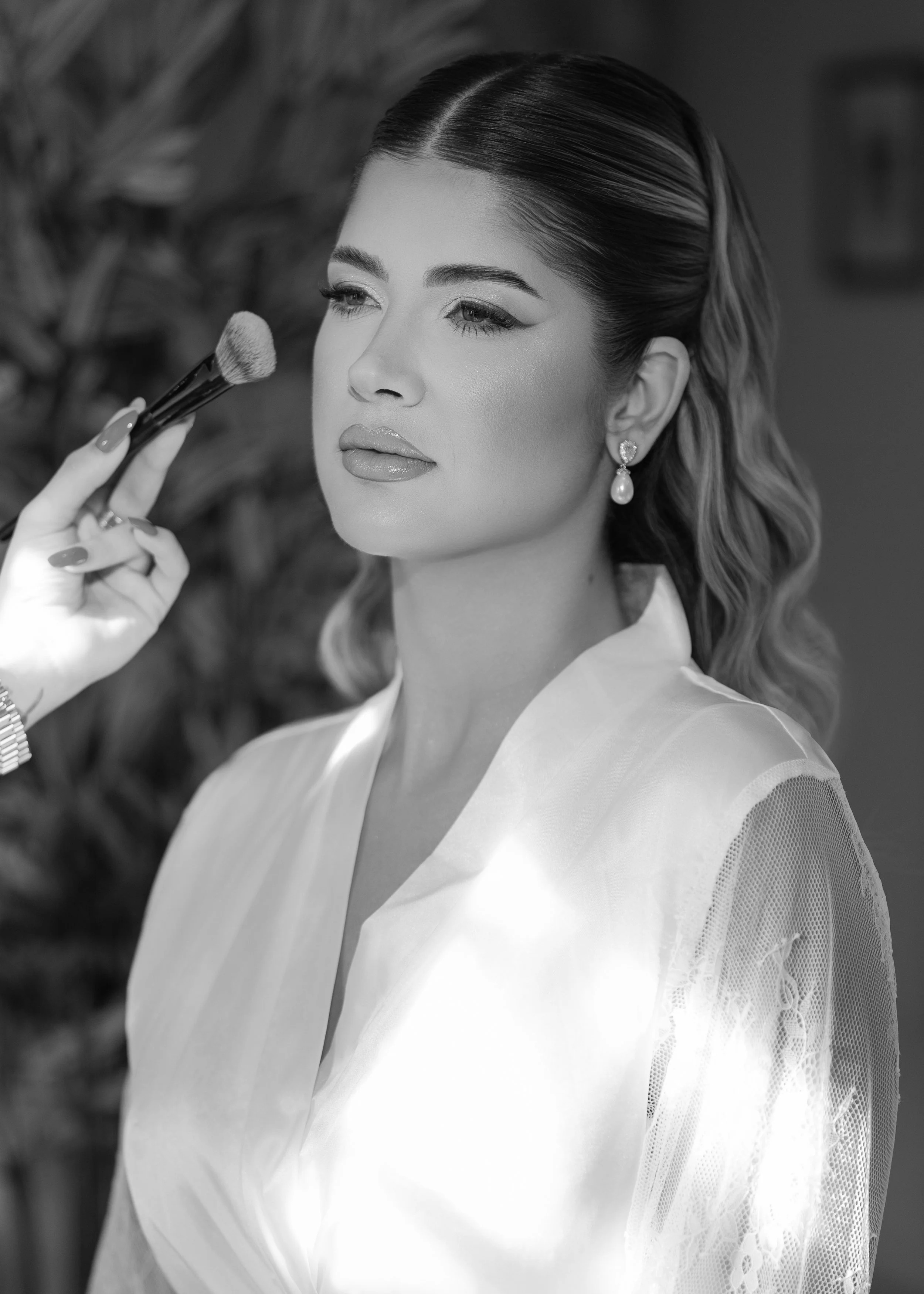 A woman with styled hair and earrings getting her makeup applied with a brush.