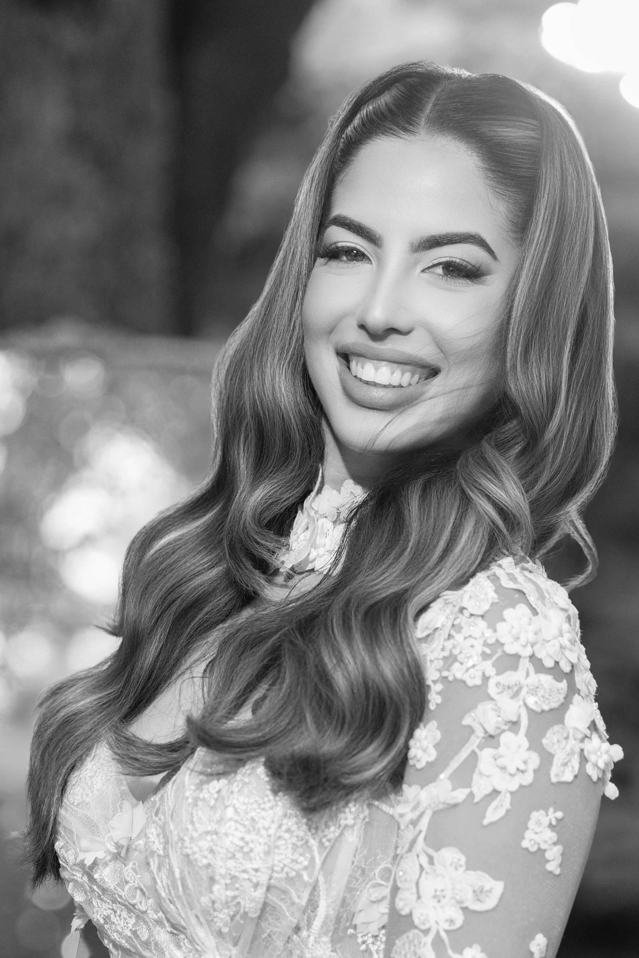 Black and white photo of a woman smiling, with long wavy hair and an embroidered dress.