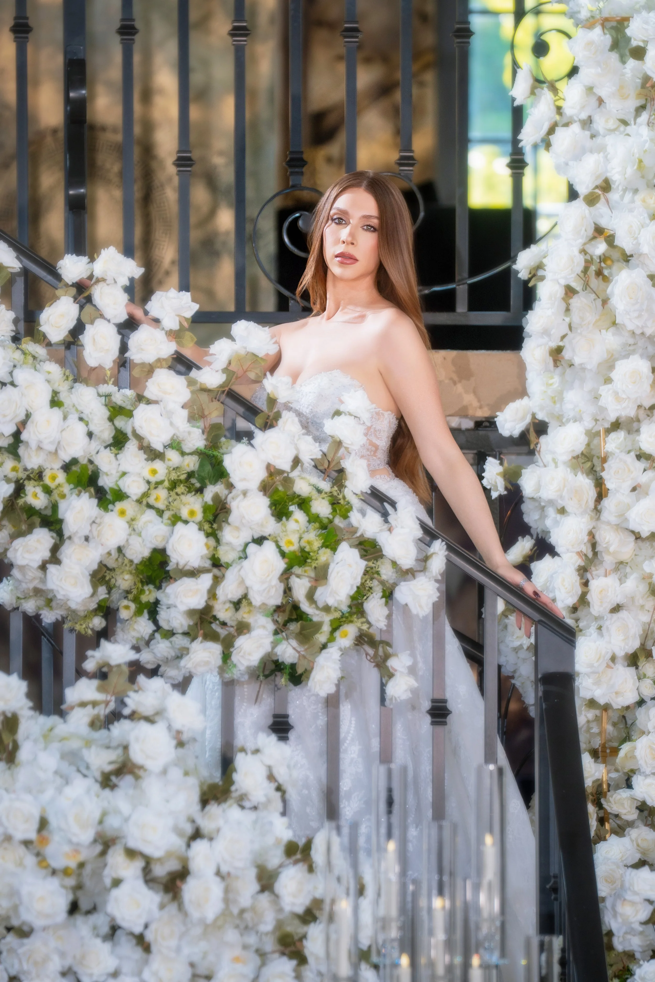A woman in a white wedding gown posing on a staircase surrounded by white flowers.