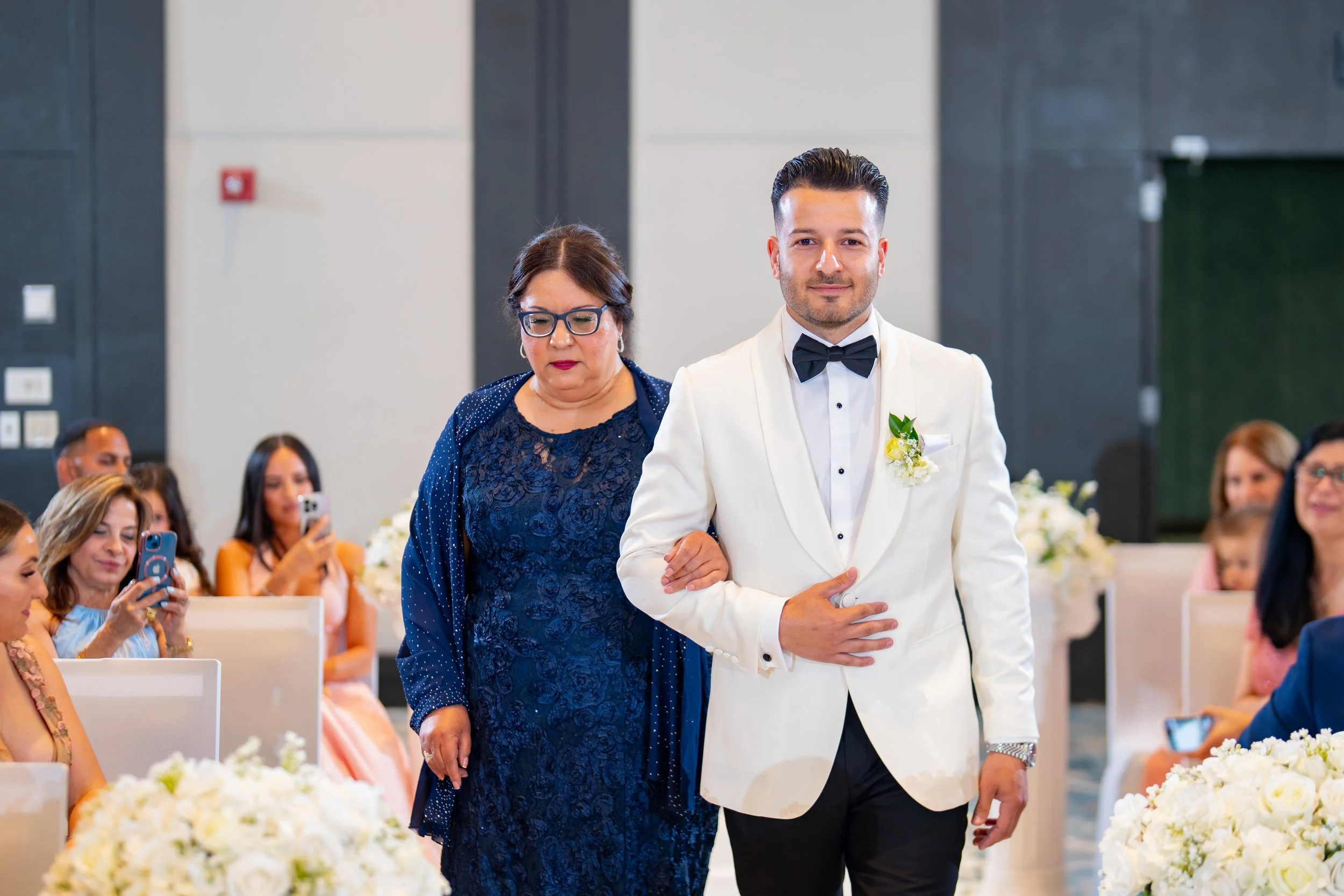 Groom's grand entrance in a white tuxedo at HILTON TAMPA DOWNTOWN; professional wedding ceremony photography by Star Visual Art, Tampa.
