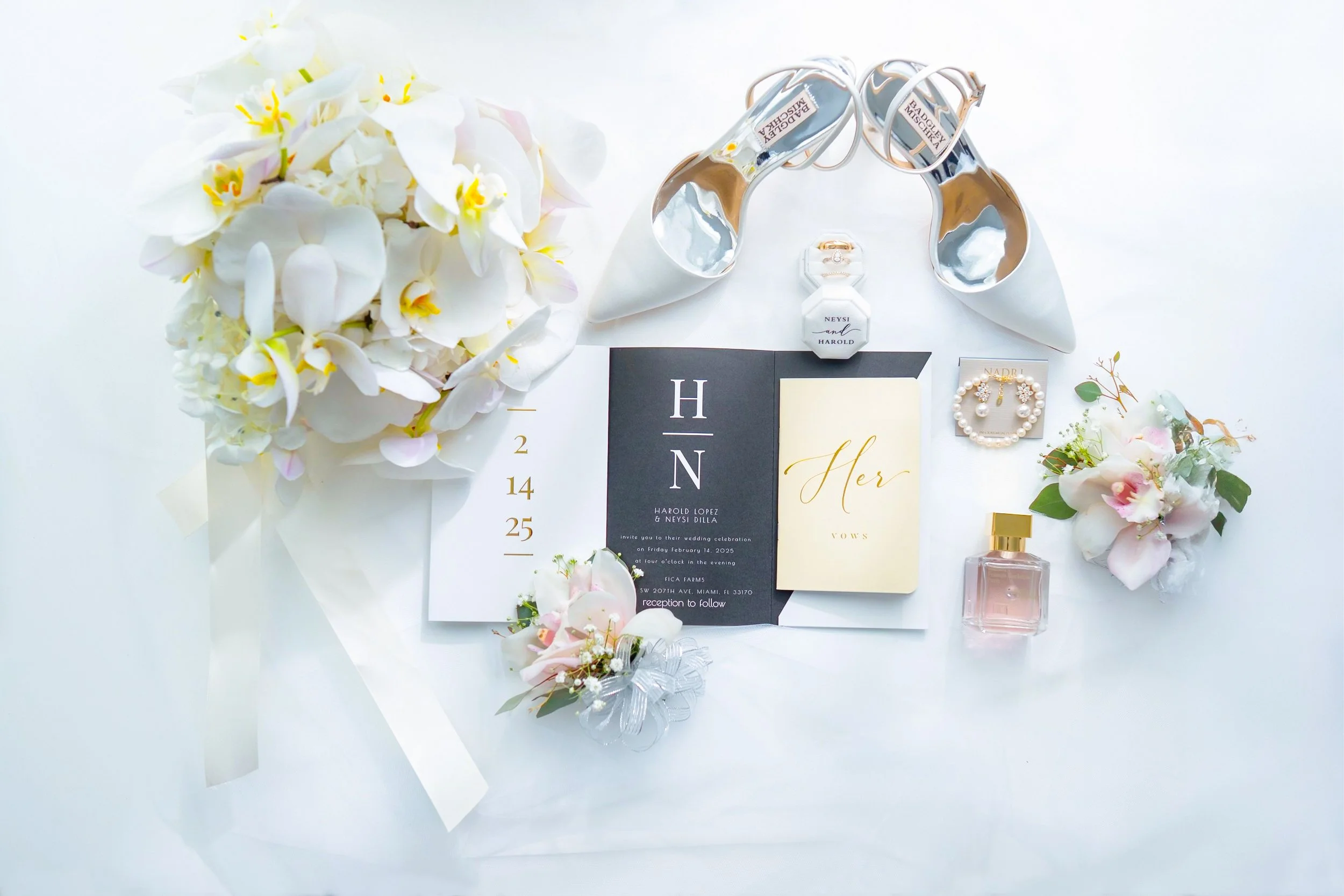 Wedding invitation suite with flowers, perfume, jewelry, and shoes on a white background.