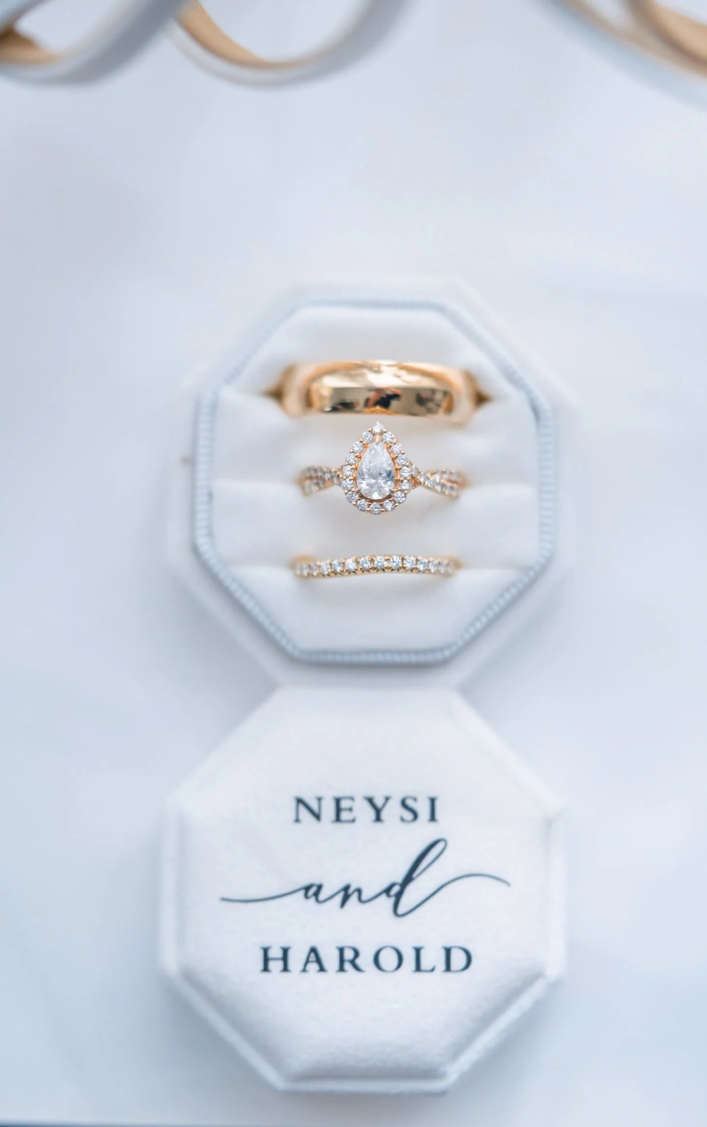 Close-up of three gold jewelry rings, two with diamonds, placed inside a white jewelry box with the words "NEYSI and HAROLD" printed inside.