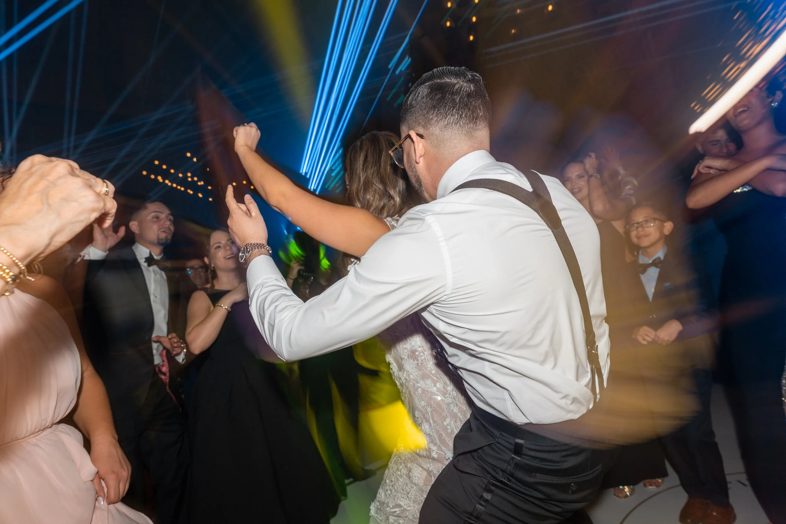 People dancing and celebrating at a party, with colorful lights and laser effects overhead.