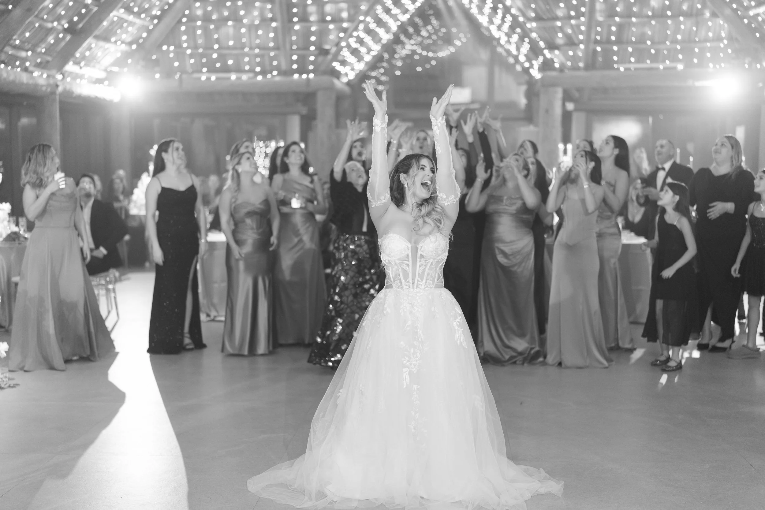 Bride in wedding gown dancing joyfully at her wedding reception with guests in the background.