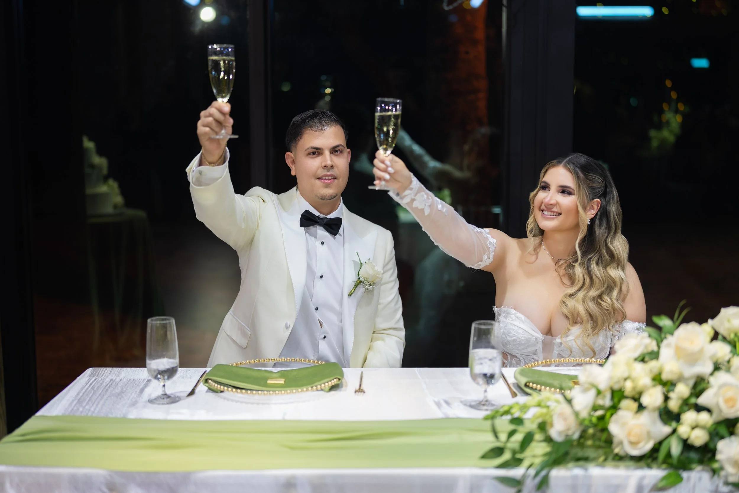Bride and groom at wedding banquet raising champagne glasses in celebration