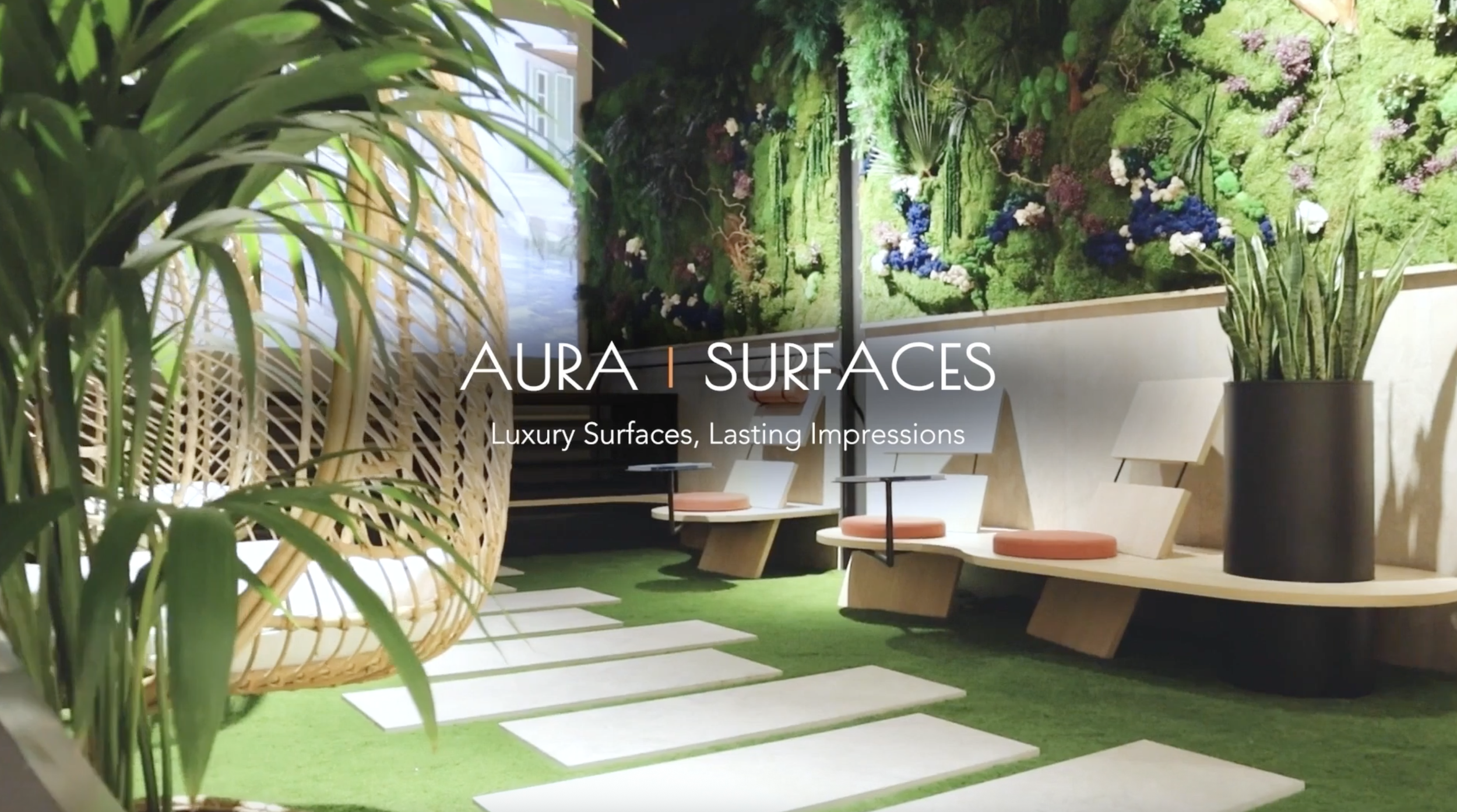 Indoor space with a lush green wall of plants, a large potted plant, modern seating with orange cushions, and a patterned bamboo hanging chair on a grassy floor with white stepping stones.