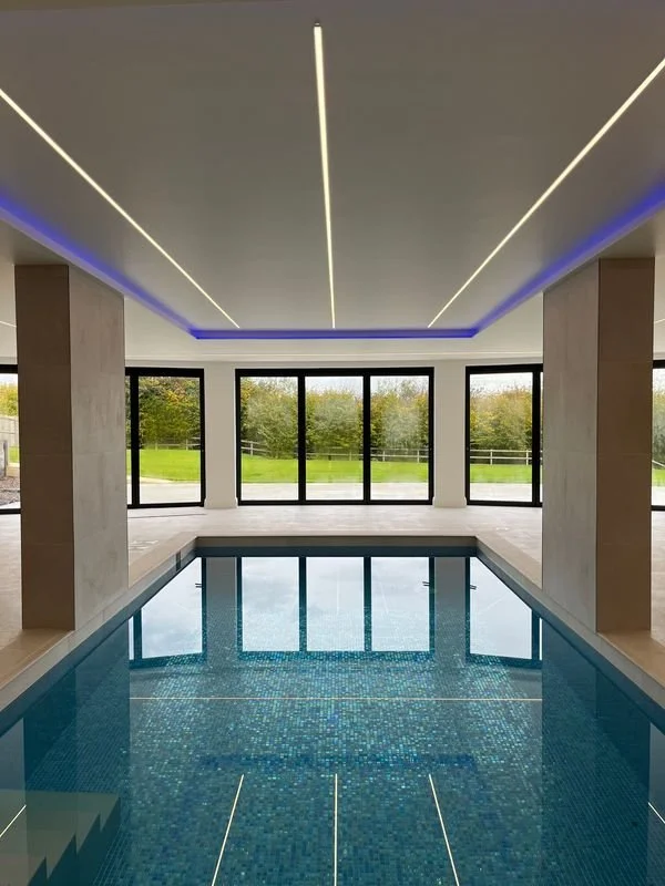 Indoor swimming pool with tiled floor and large windows showing a green outdoor landscape