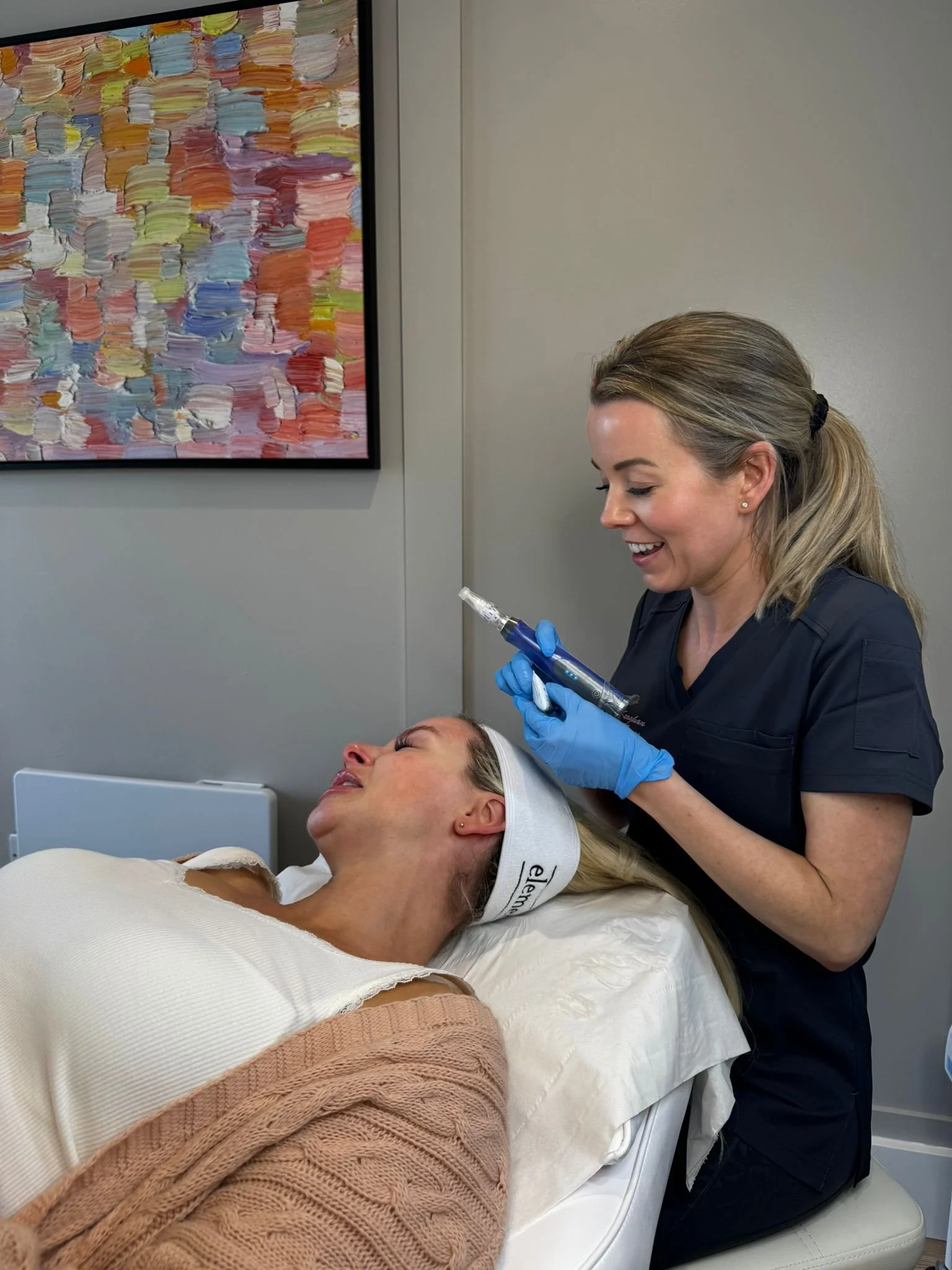 A woman lying on a medical bed receiving a cosmetic injection from a nurse in a clinical setting.