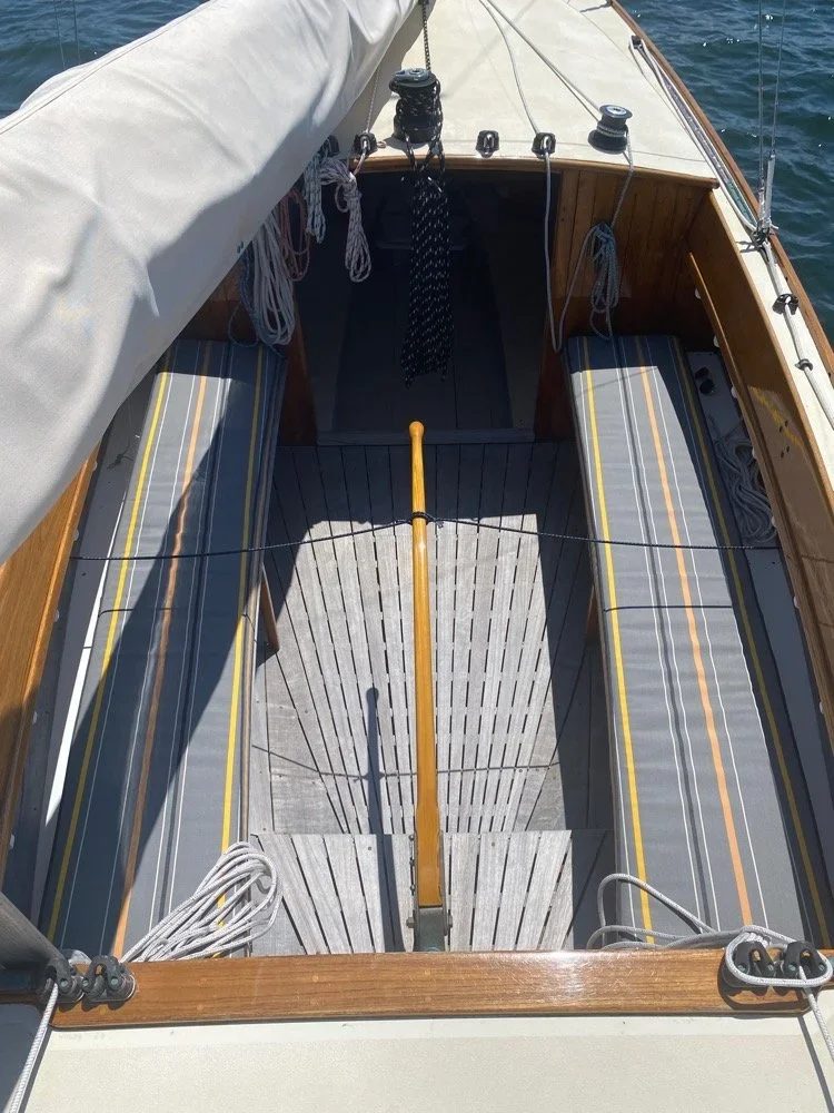 Top-down view of a small sailboat with striped cushions, wooden deck, and sailing equipment on a body of water.