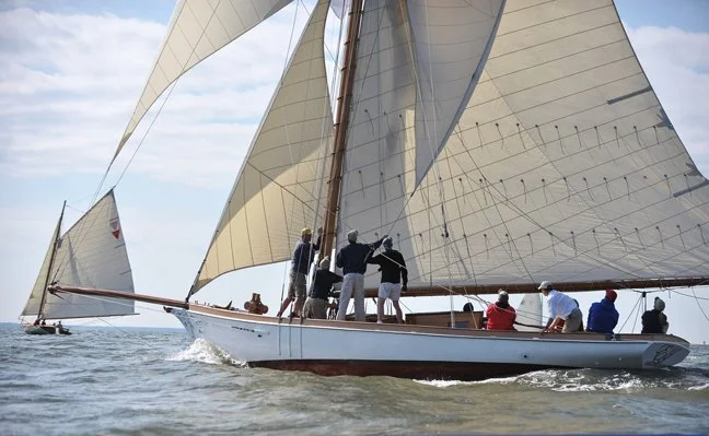 A sailboat with large white sails sailing on the water with people on board.