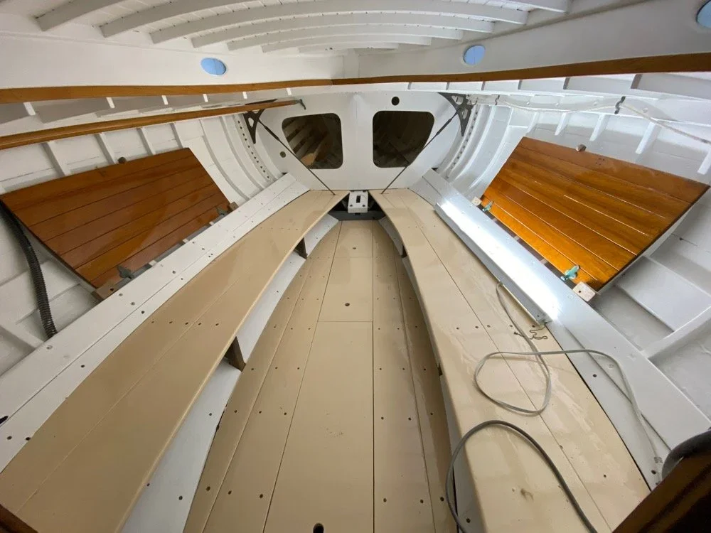 Interior of a boat or ship under construction, showing wooden and beige panels, white walls, and a curved ceiling with support beams.
