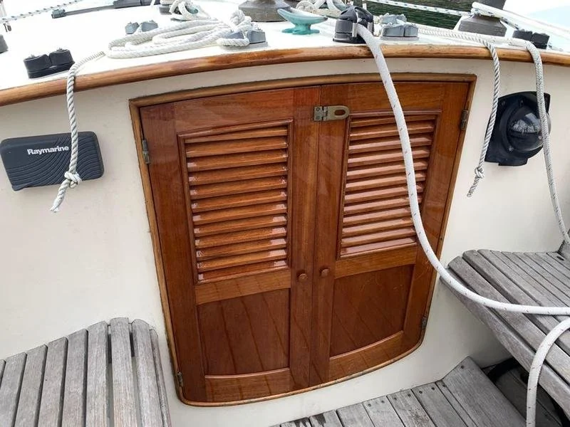Wooden boat hatch with louvered doors, surrounded by boat equipment like ropes, a Raymarine device, and a wooden bench.