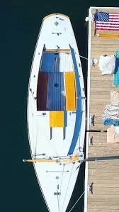 An overhead view of a white paddleboard with yellow, blue, and brown bags on it, positioned on a dock next to a beach area with clothes and towels.