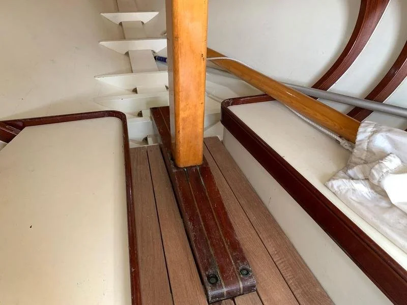 Close-up of a boat interior showing two cushioned seats on either side, a wooden support beam, a set of white curved stairs, and a metal railing.