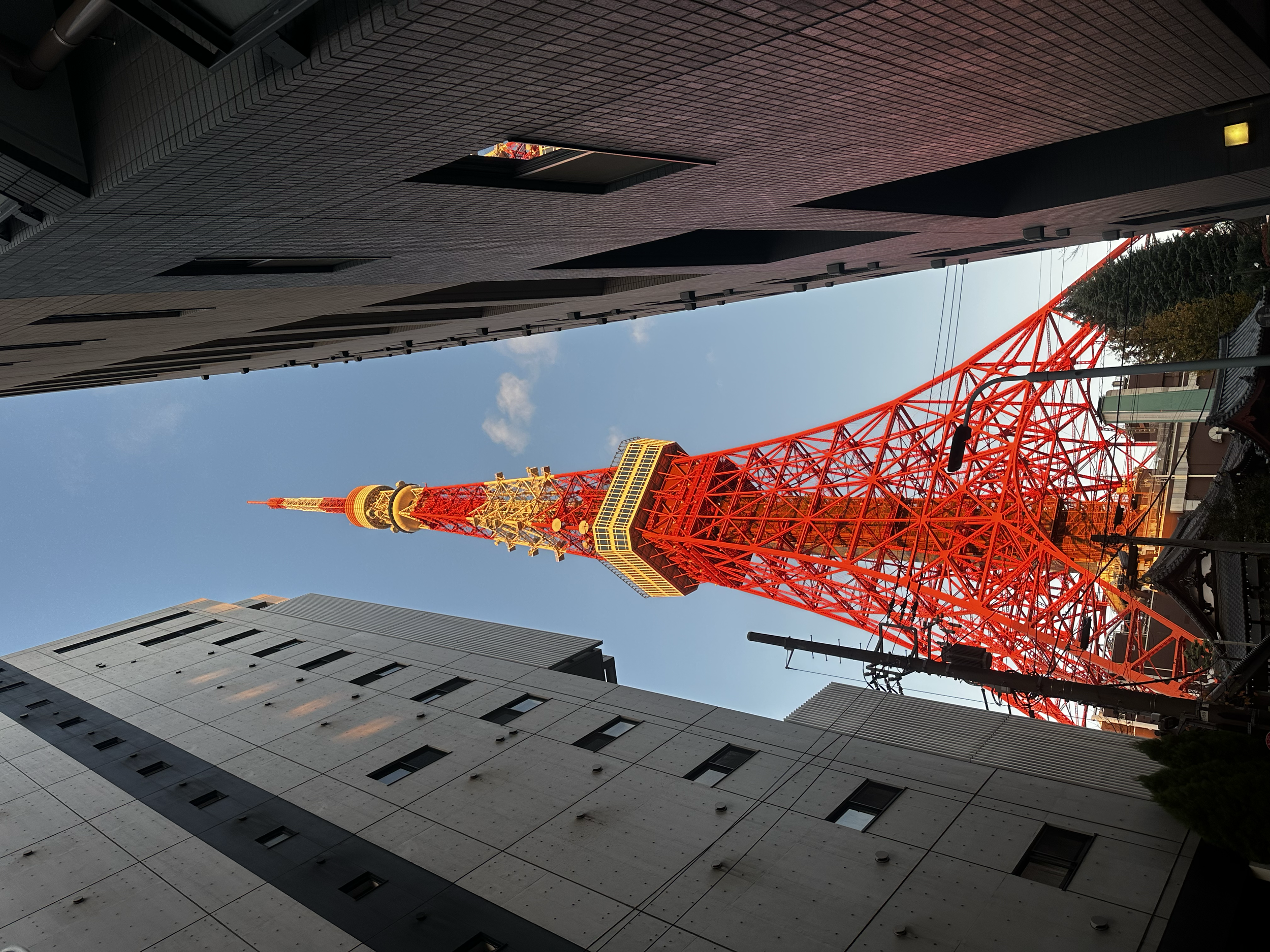 Une tour en treillis rouge vif entre deux bâtiments modernes, vue de bas en haut, contre un ciel bleu clair.