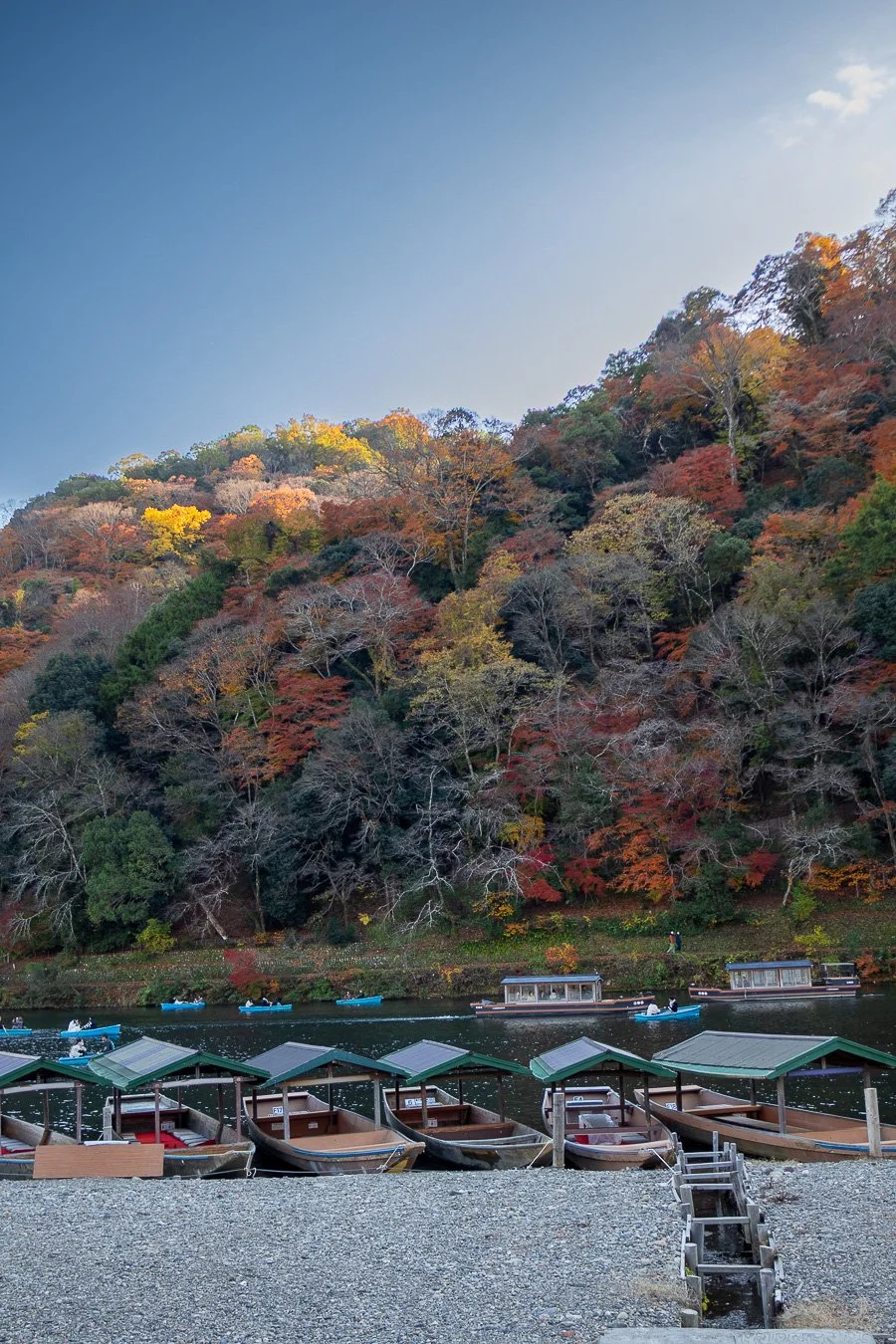 Bateaux en bois avec toits verts amarrés au bord d'une rivière, avec une forêt d'automne aux arbres colorés en arrière-plan.
