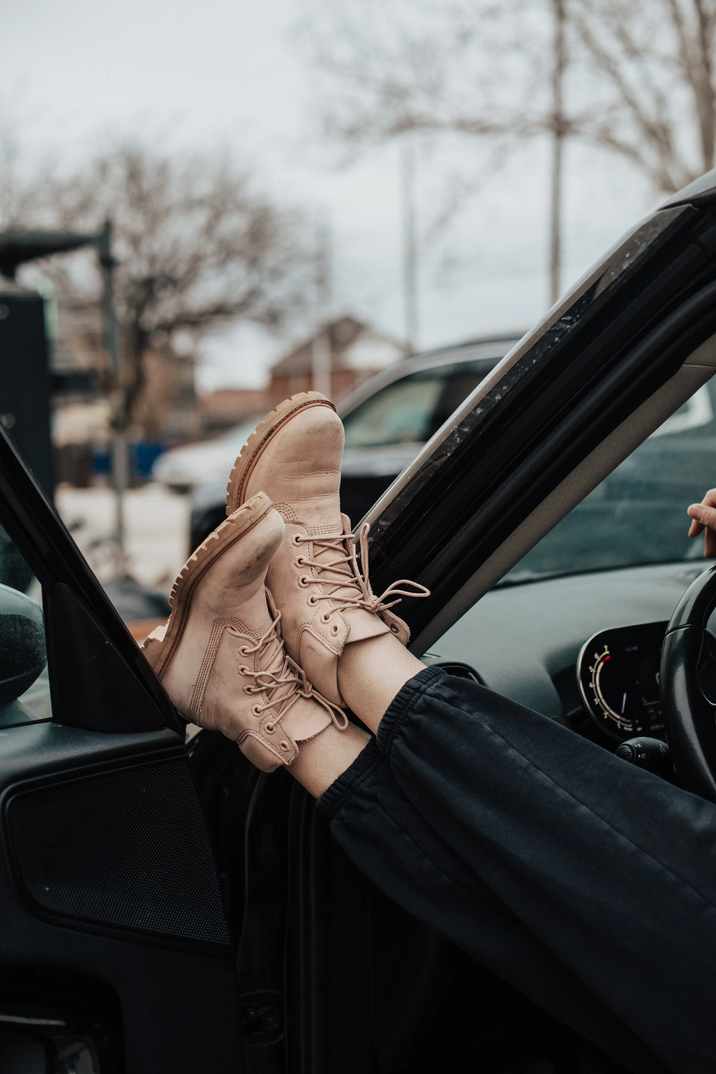 Person with legs extended, wearing beige boots, resting their feet on the open car door inside a vehicle.