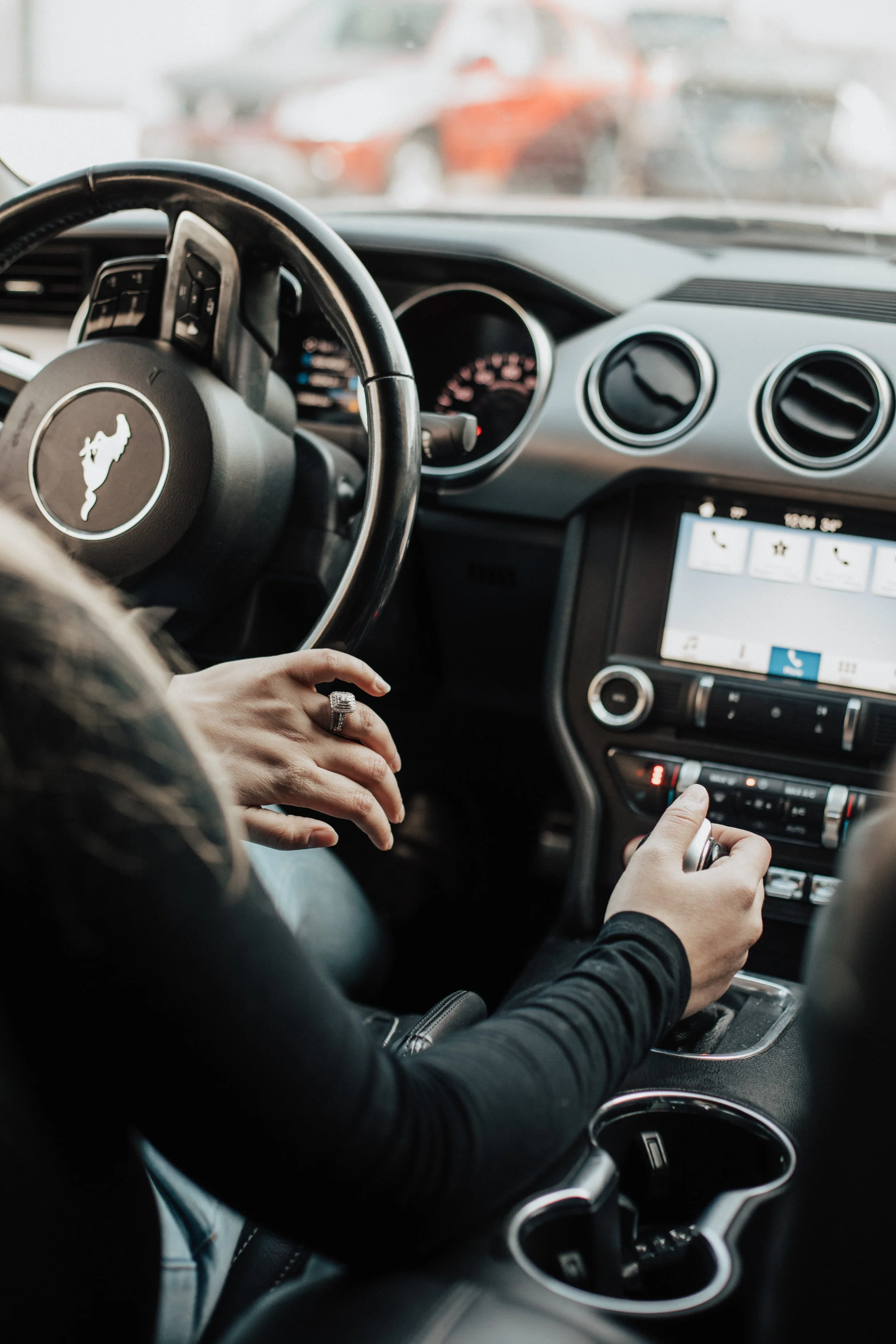 Interior of a Ford Mustang with a woman’s hand on the gear shift and her other hand resting on the steering wheel.
