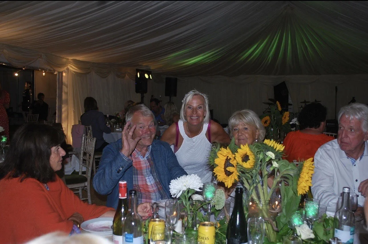 People sitting at a dining table with sunflower centerpieces inside a decorated marquee for a 60th birthday party in Dunsfold Surrey Cranleigh