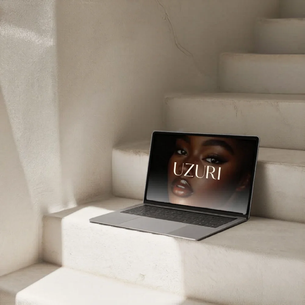 A laptop on white stairs with a close-up image of a woman's face on the screen and the text 'UZURI' over her face.