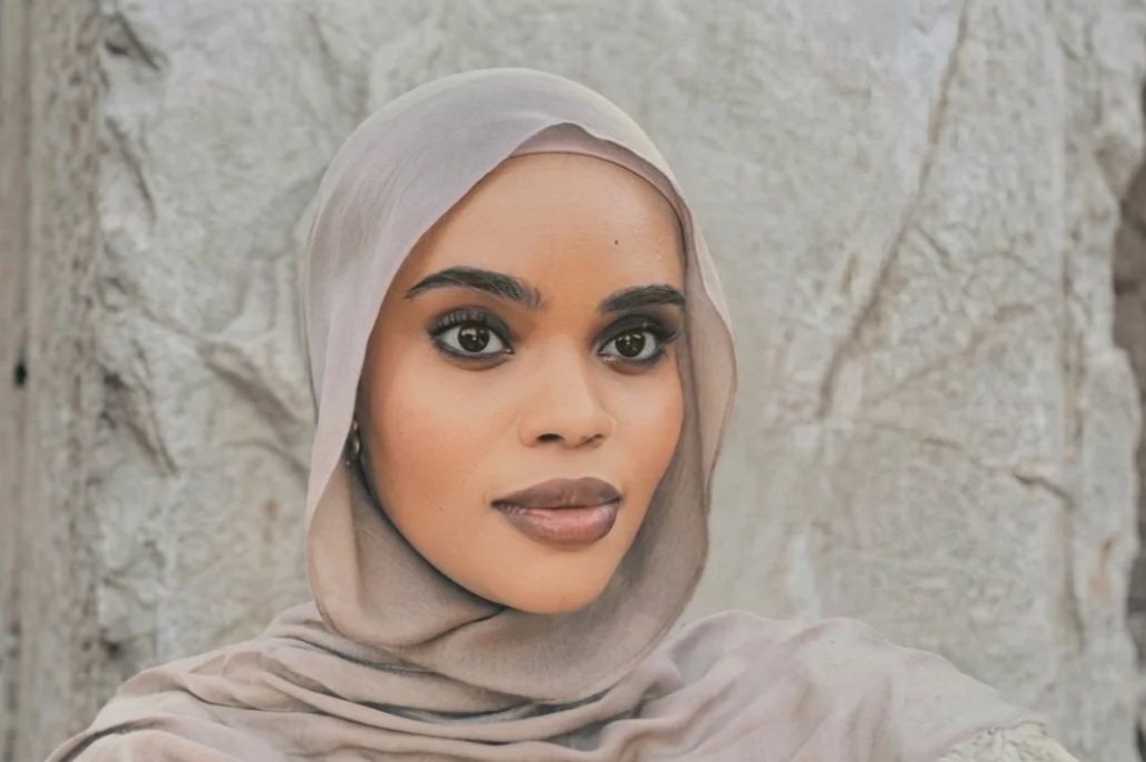 Close-up of a woman wearing a light beige hijab in front of a textured stone wall