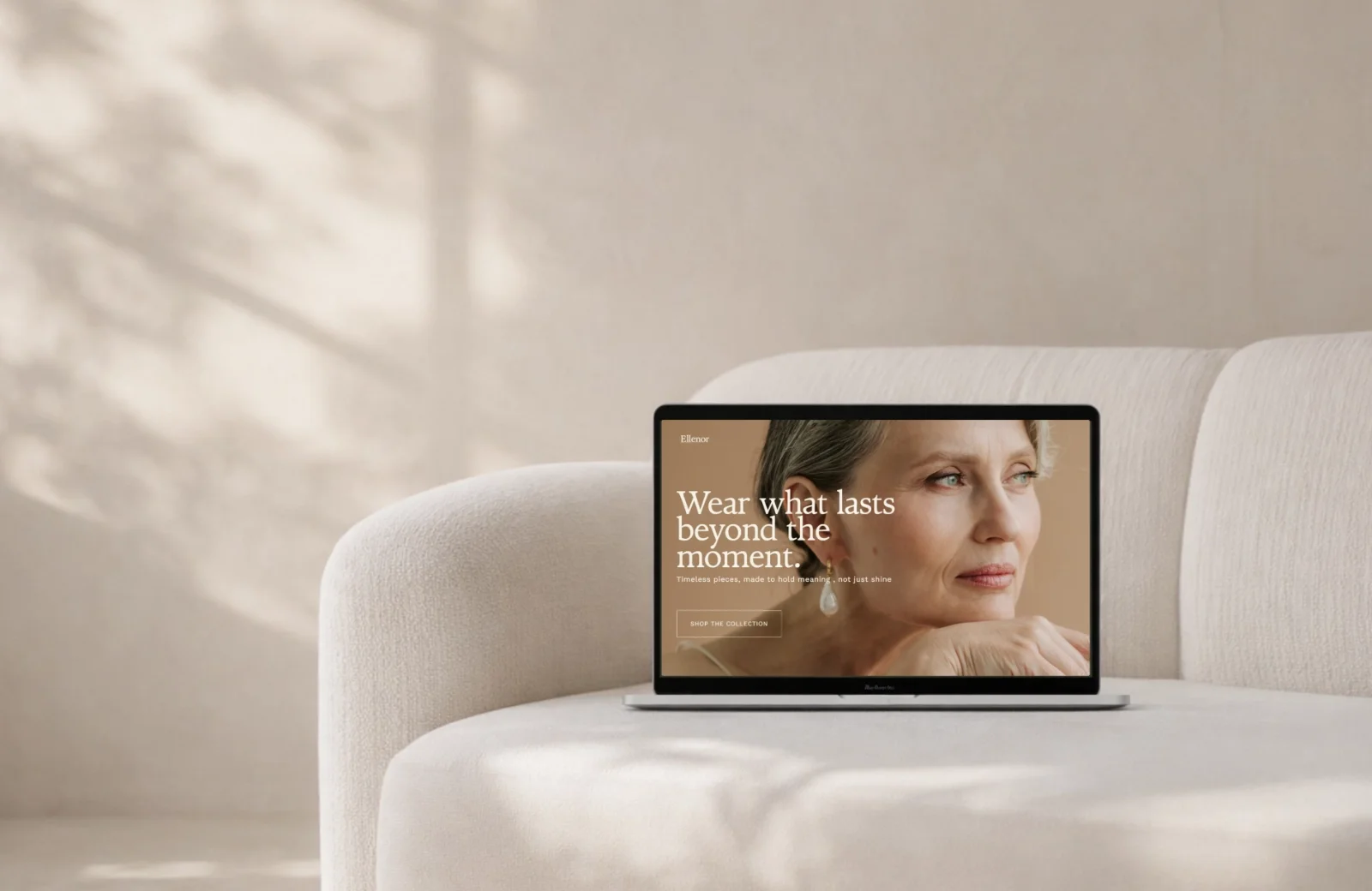 A laptop displaying a website with an older woman wearing pearl earrings and a beige top, sitting against a neutral background.