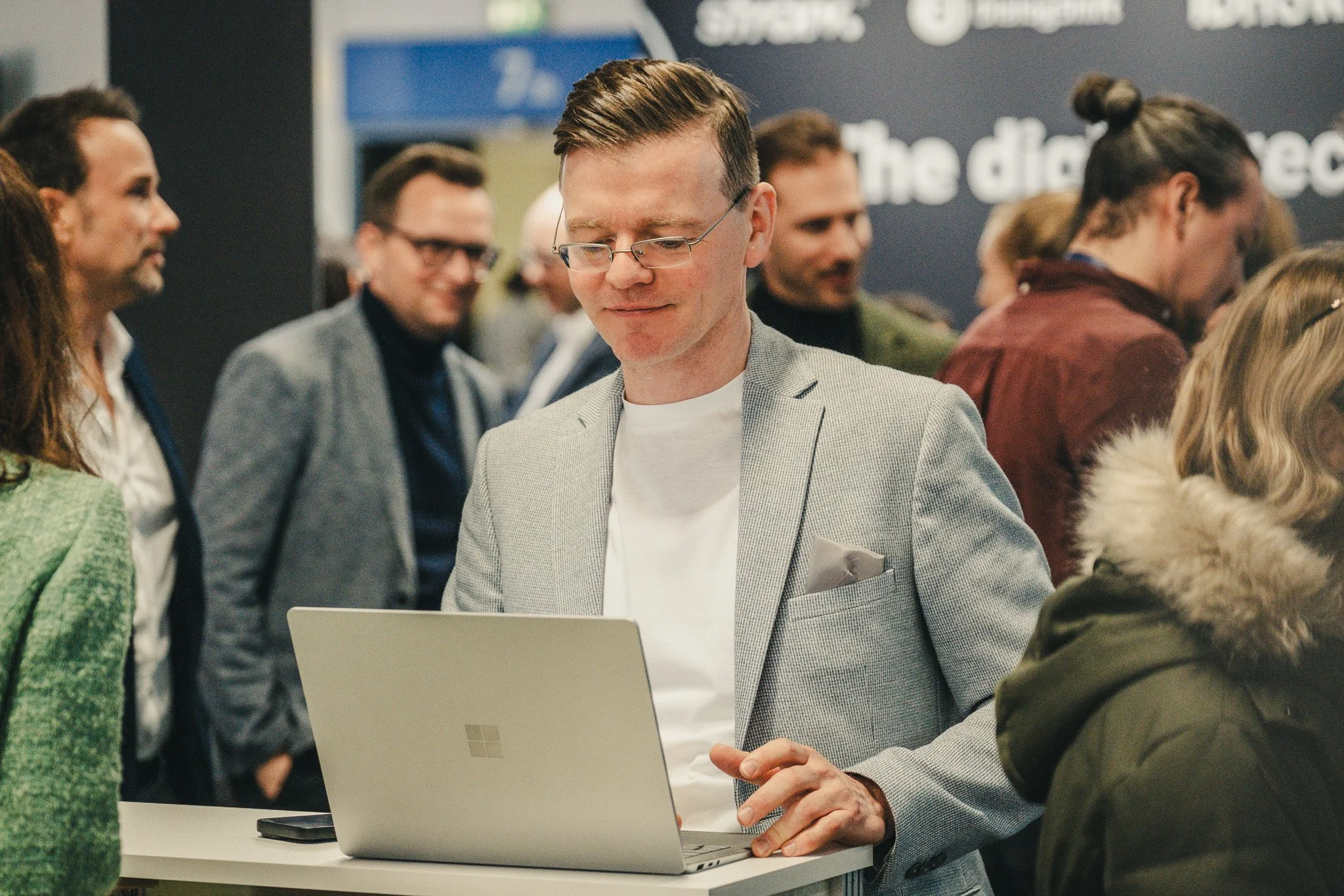 Bernd Fritzges using a laptop at an industry event, surrounded by attendees networking in the background