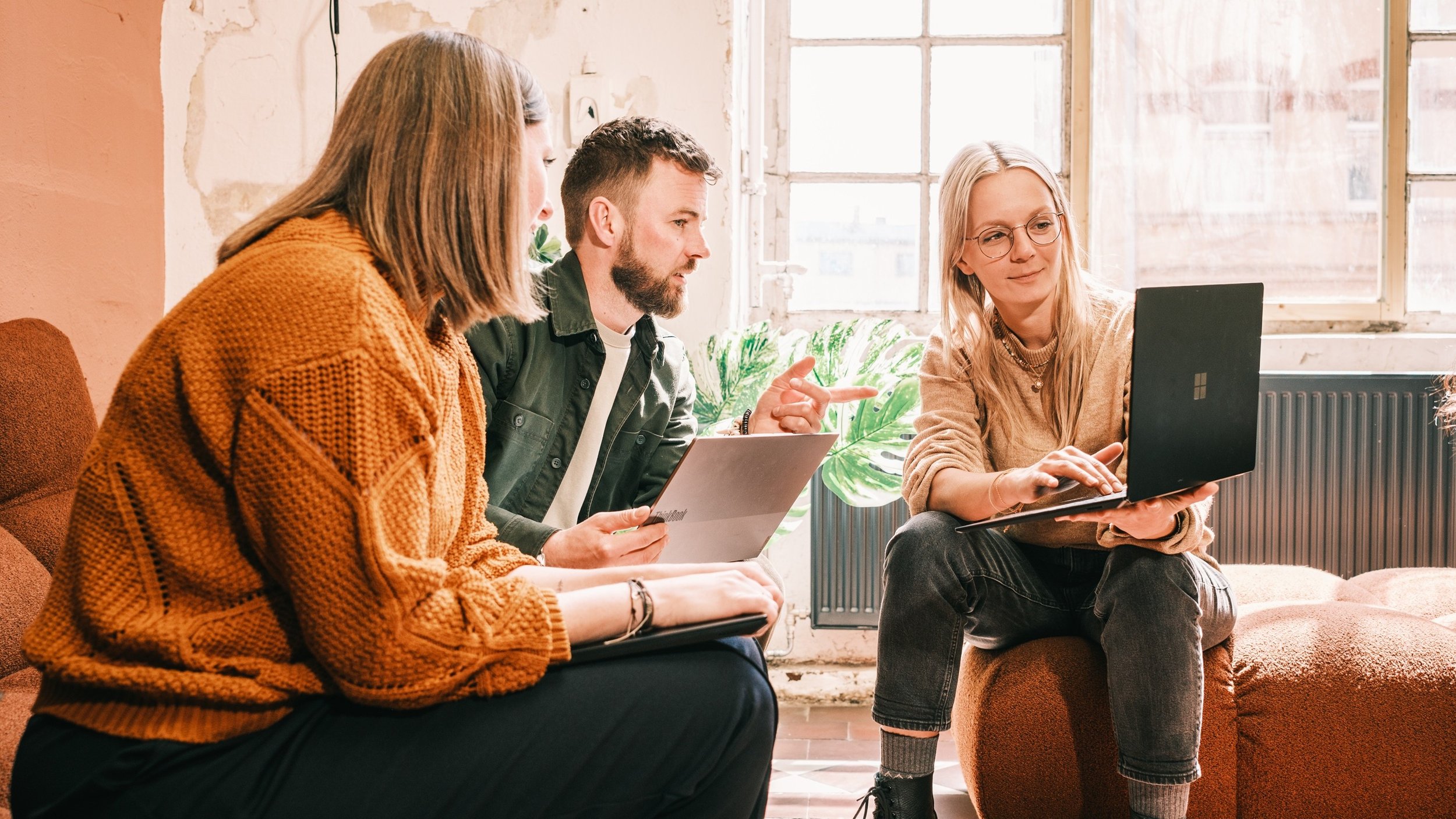 Three colleagues sitting together in a meeting, discussing and reviewing information on a laptop