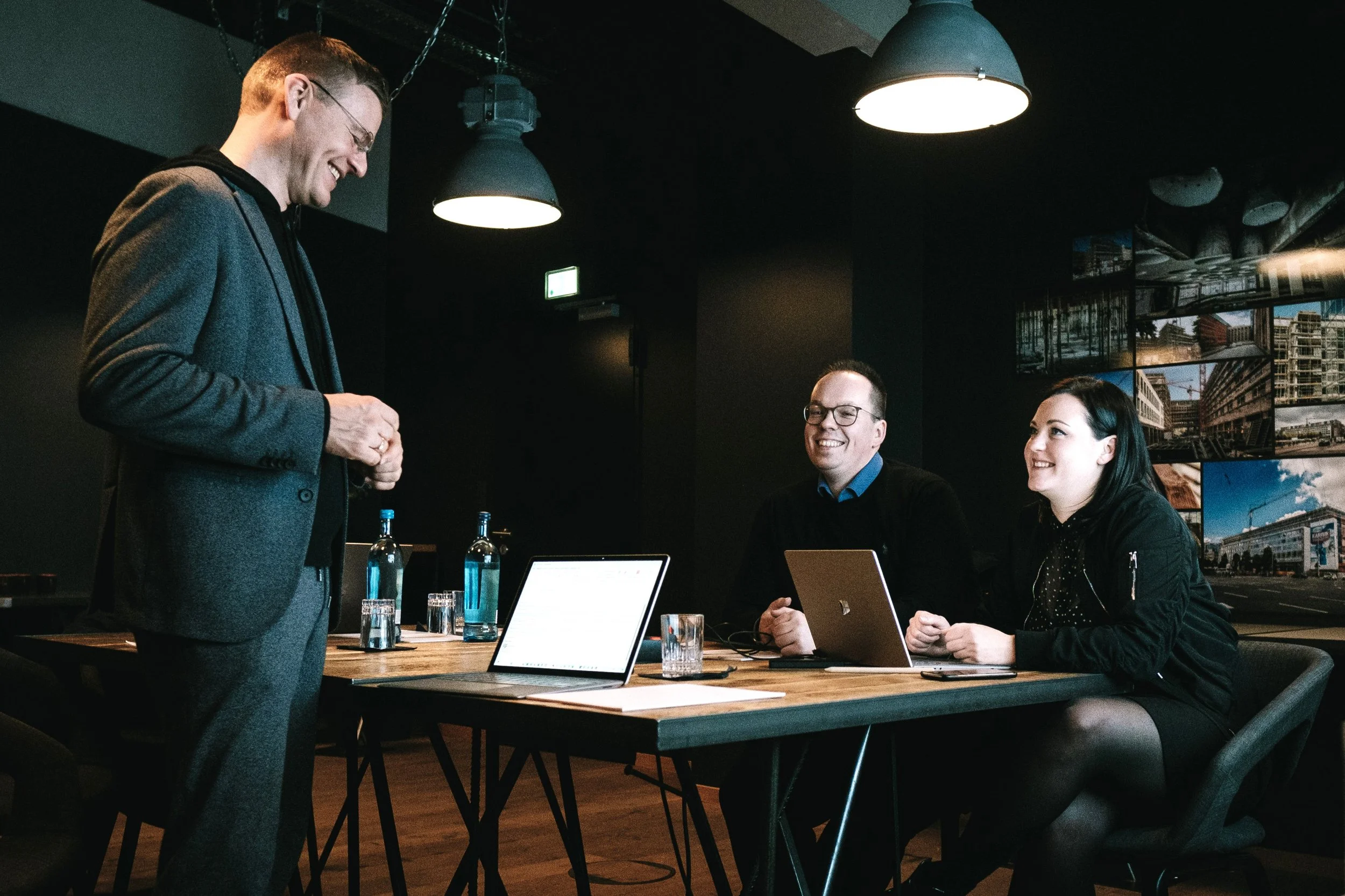 Three people are sitting at an office desk and talking to each other.