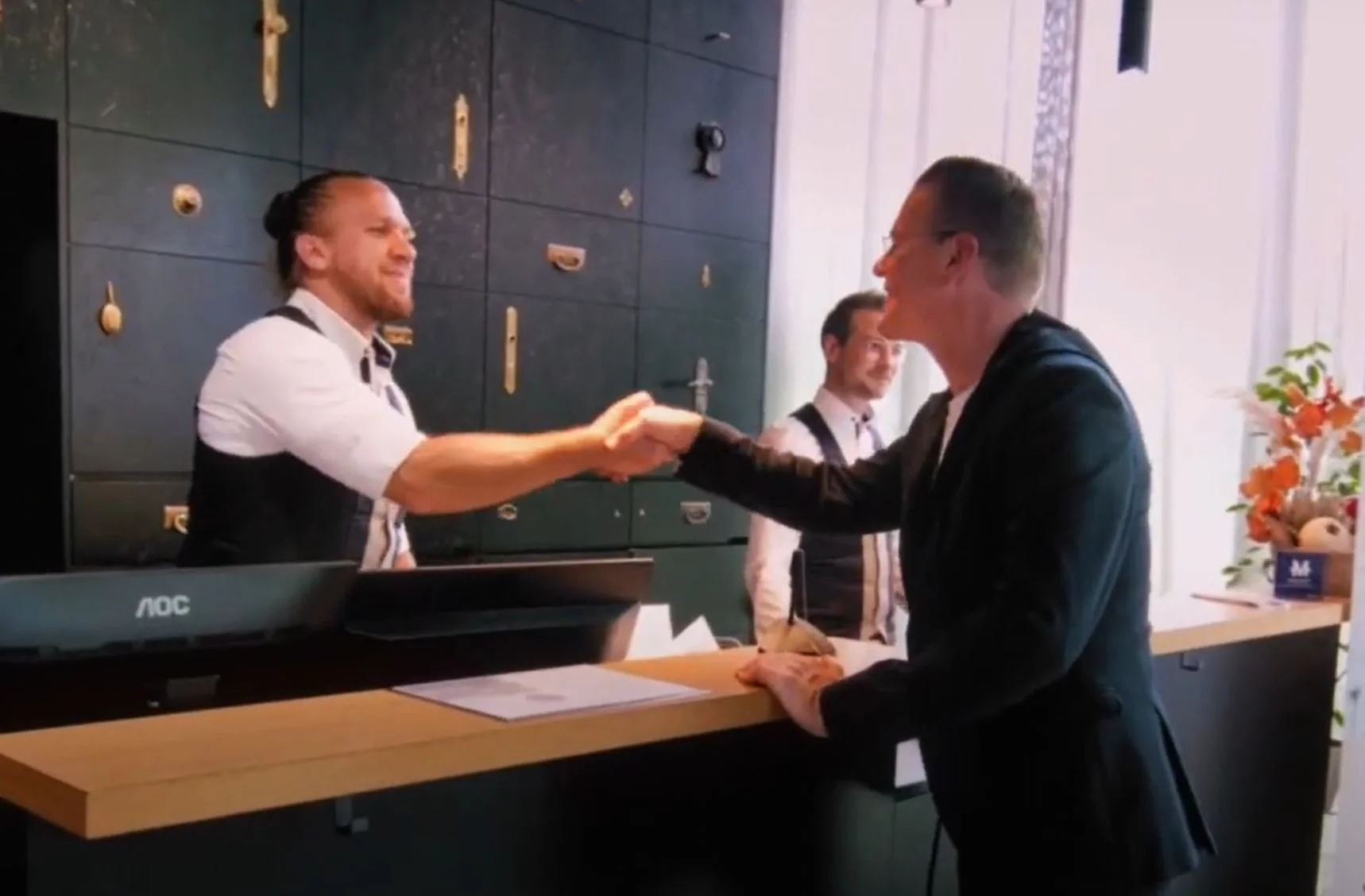 Hotel receptionist greeting Bernd Fritzges with a handshake at the front desk during check-in