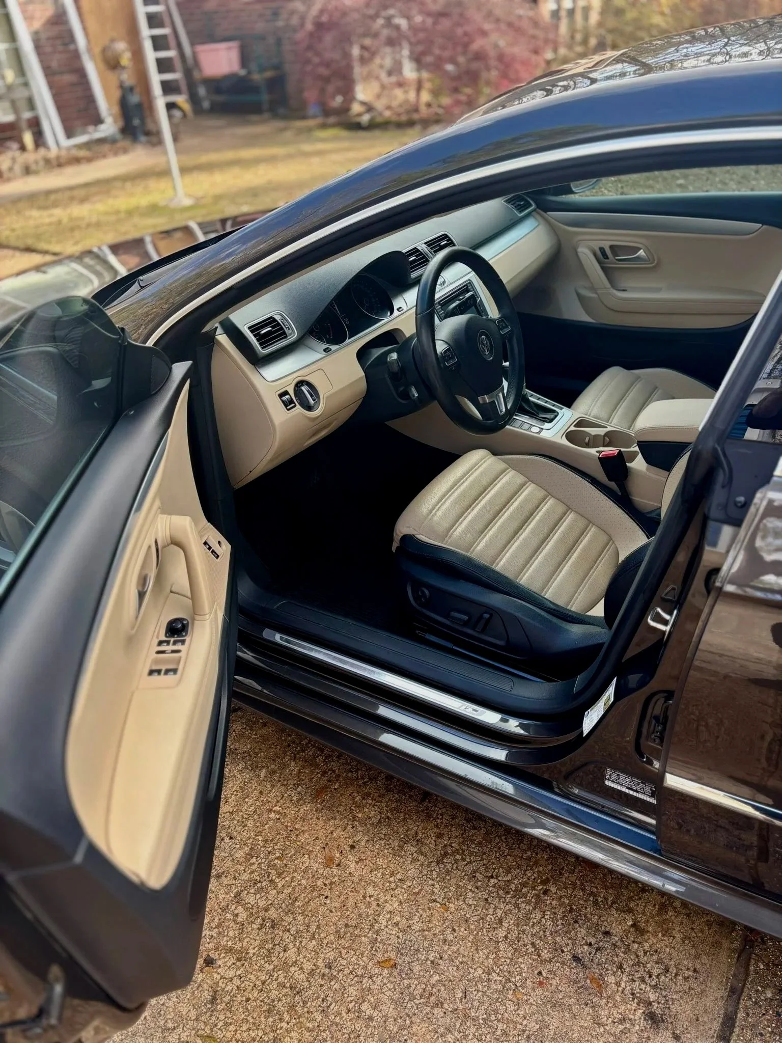 Interior of a black car with beige seats, showing the driver's side with the door open, dashboard, and steering wheel.