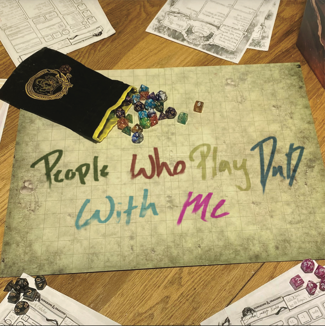 A tabletop gaming setup with colorful dice spilling out of a black dice bag onto a grid paper mat with the phrase “People Who Play DnD With Me” written in colorful letters. Created by graphic design student Kenzie Coates for a sophomore design class.