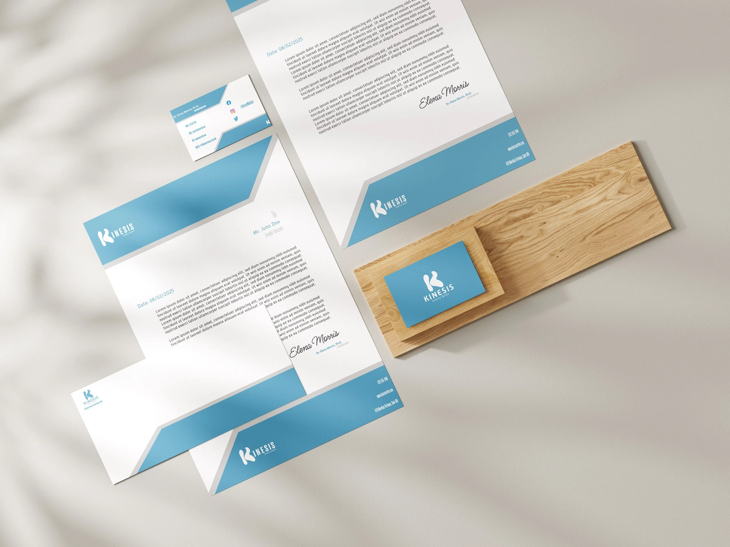 Business stationery including letterhead, envelope, business card, and a wooden desk block, all with blue and white branding for Kinesis. Created by graphic design student Kenzie Coates