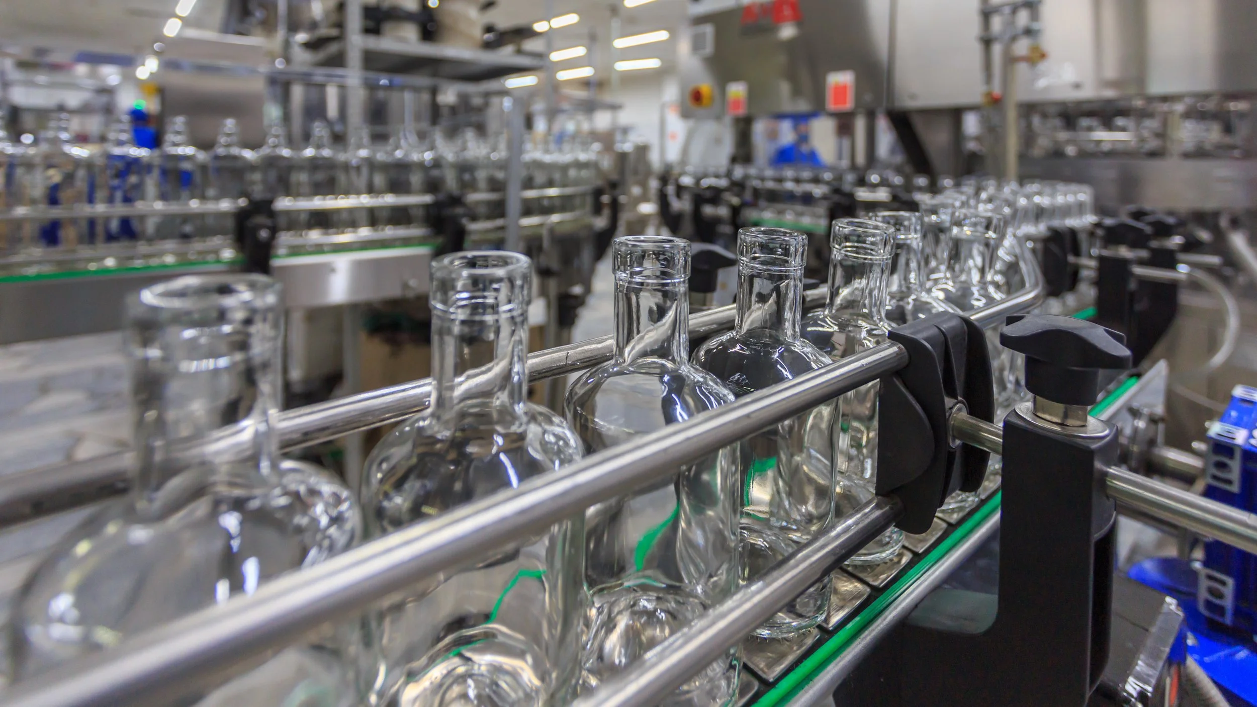 Empty glass bottles being transported on a conveyor belt in a manufacturing or bottling plant.