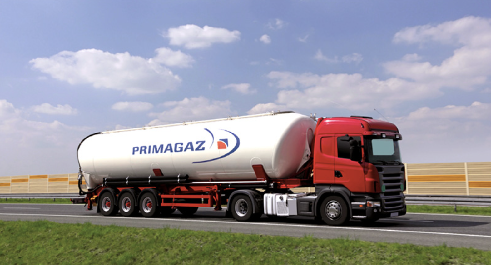 Un camion de transport de gaz avec un réservoir blanc marqué PRIMAGAZ, sur une route avec un ciel bleu et quelques nuages.