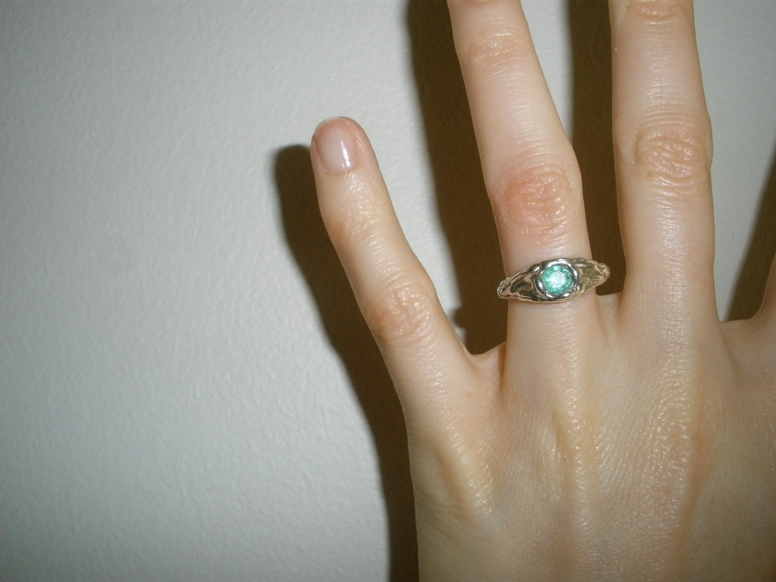 Close-up of a hand wearing a silver ring with a green gemstone on the middle finger