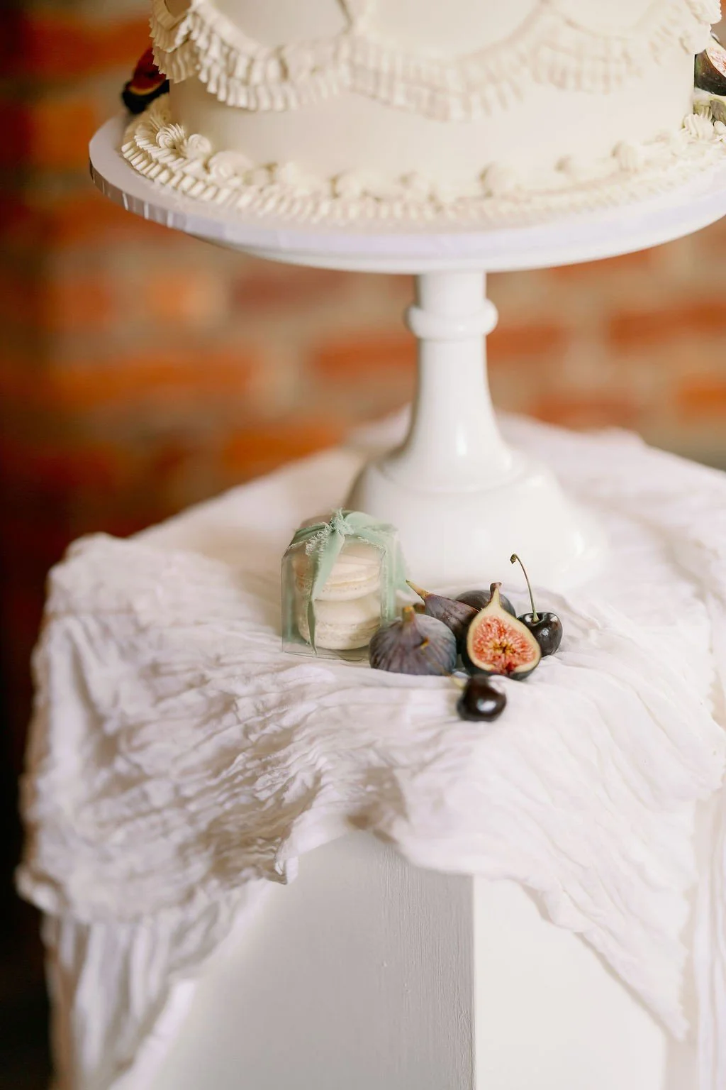 A box of macarons tied in a sage green bow, sitting under a wedding cake and surrounded by fresh fruits.