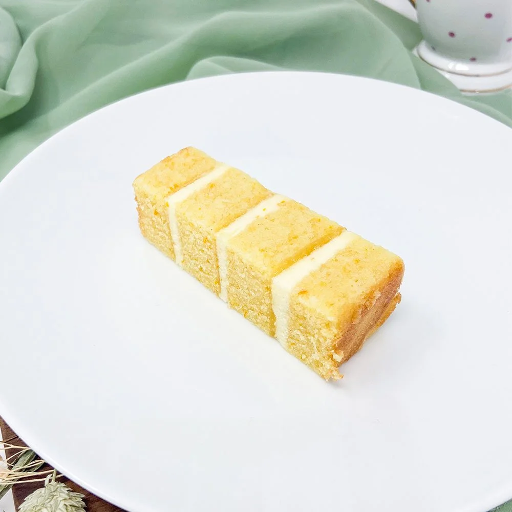 A slice of yellow cake with white icing on a white plate.
