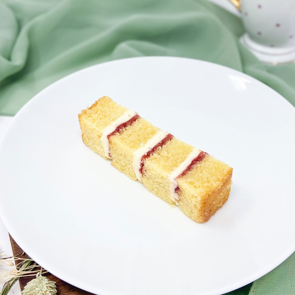 A slice of layered cake with white icing and red filling on a white plate.